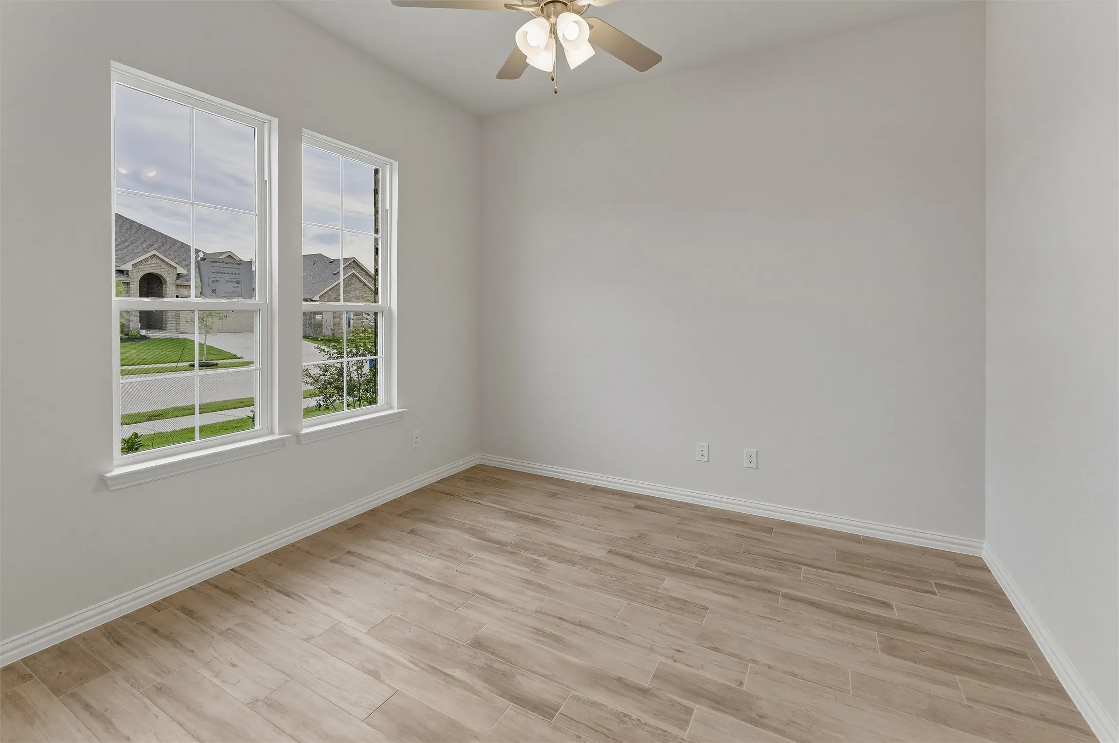 Bright room featuring two large windows, wood-finish flooring, a ceiling fan, and crisp white baseboards