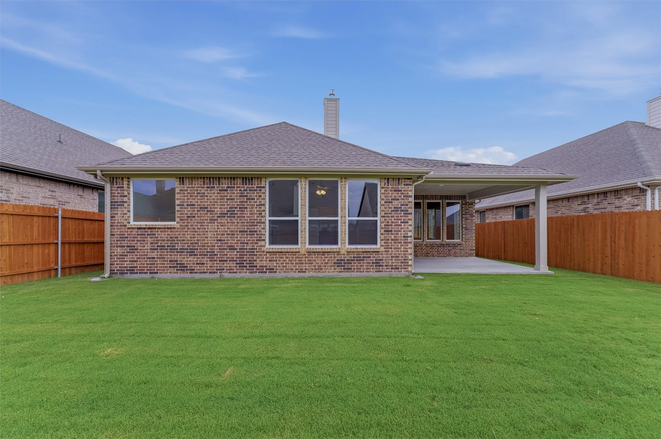 Expansive backyard featuring a manicured lawn, brick exterior, covered patio, and wood privacy fencing