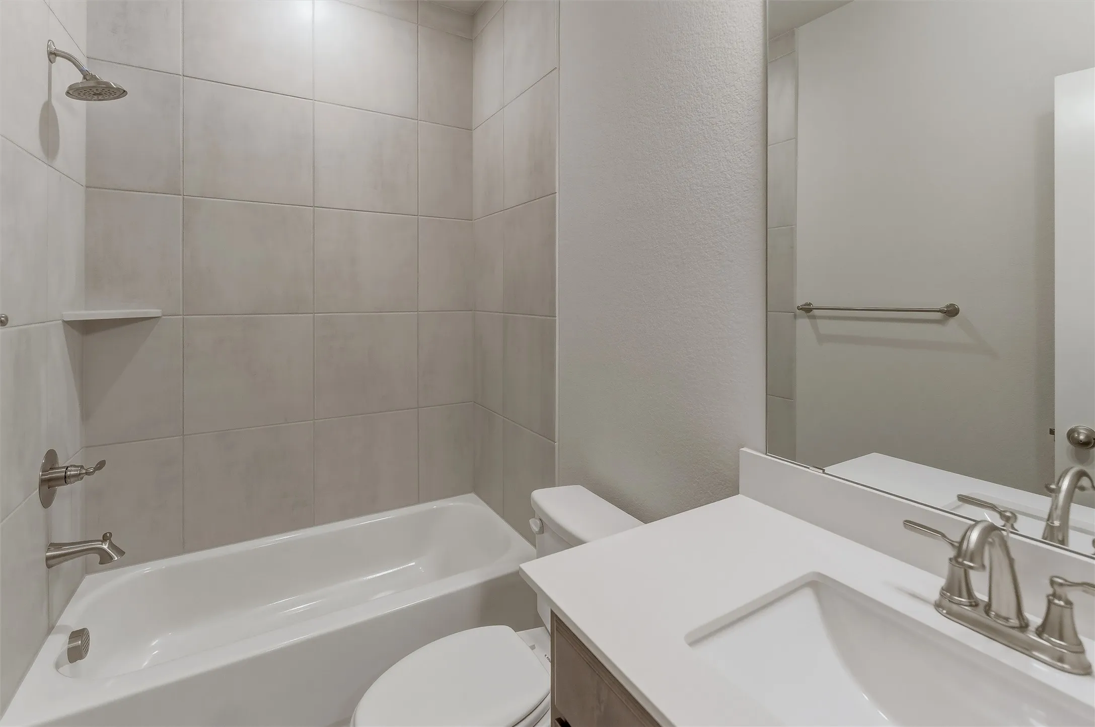 Bathroom featuring a white bathtub with a tiled surround, a toilet, a vanity with a white countertop, an undermount sink, and brushed nickel fixtures