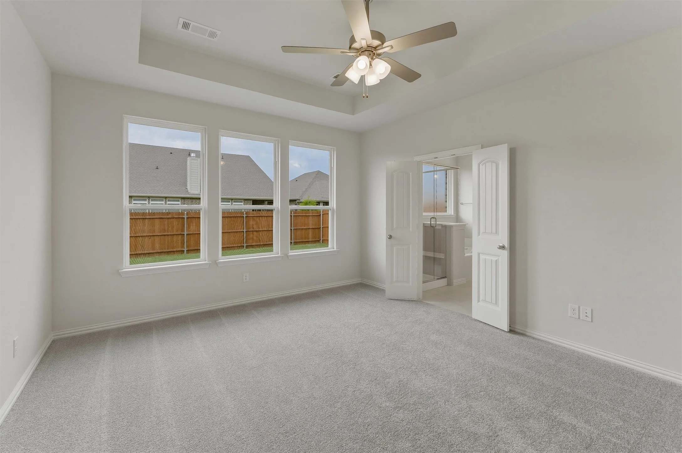 Spacious room featuring light gray carpeting, a tray ceiling with a mounted ceiling fan, and three large windows