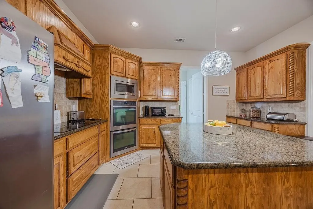 Kitchen with stainless steel appliances, dark granite countertops, tasteful backsplash, and wood finish cabinetry