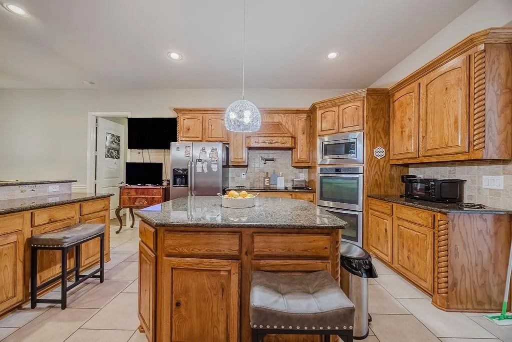 Kitchen with granite countertops, a center island, stainless steel appliances, backsplash, and decorative light fixtures