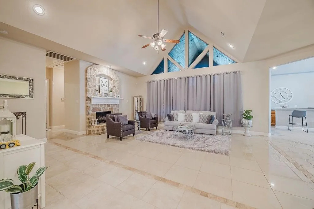 Living room with a high ceiling, inlaid floor details, a ceiling fan, light tile patterned floors, and a stone fireplace