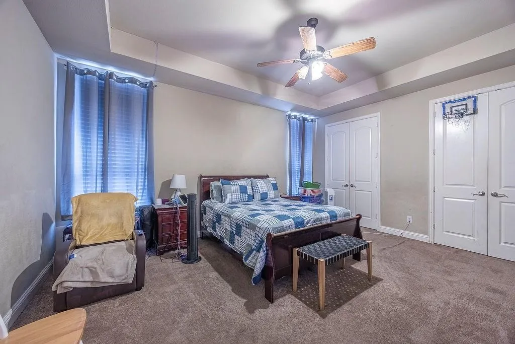 Carpeted bedroom featuring a tray ceiling, two closets, and ceiling fan