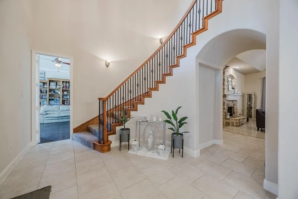 Stairs with a high ceiling, arched walkways, a ceiling fan, a stone fireplace, and tile patterned floors