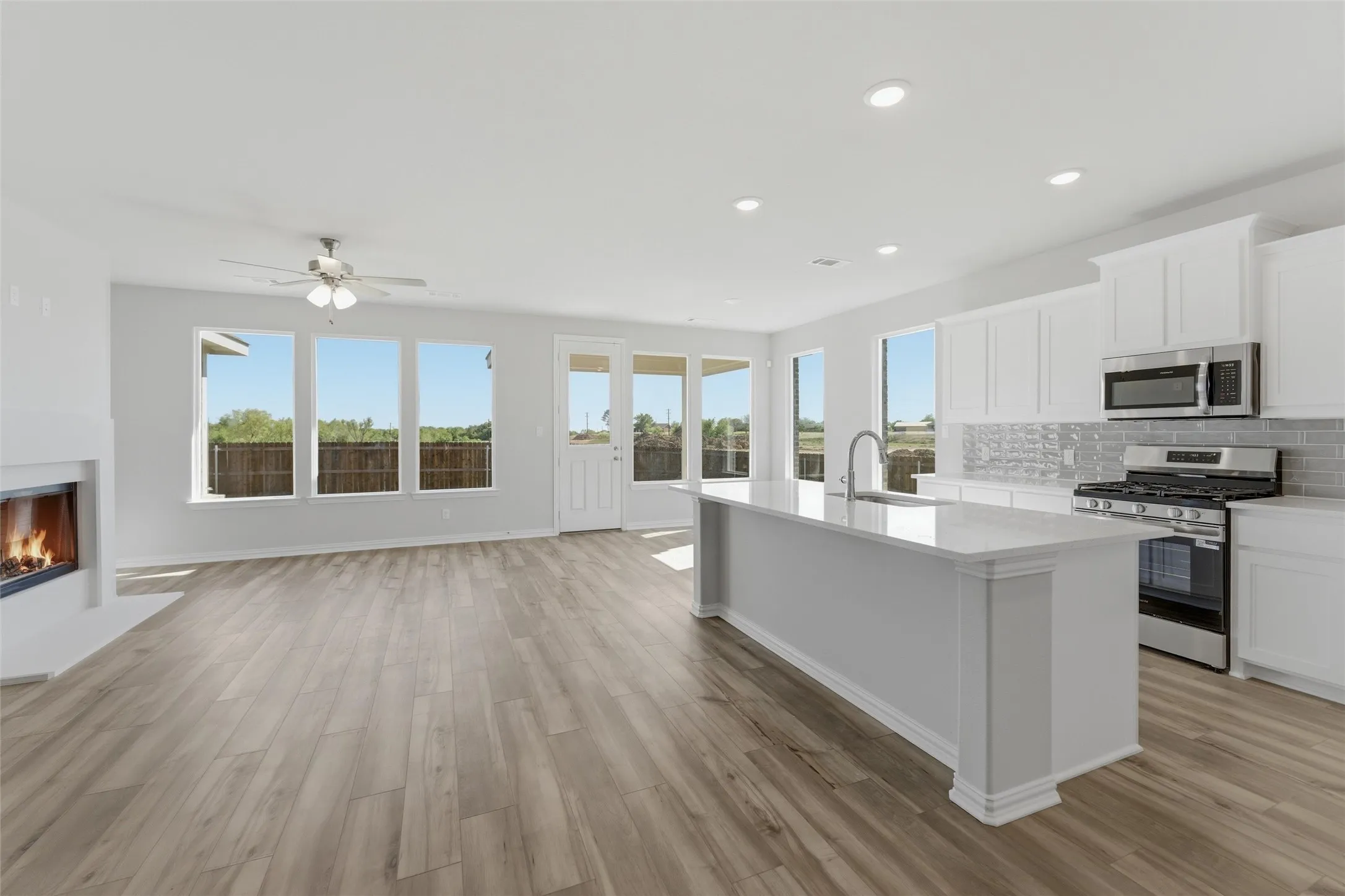 Kitchen featuring stainless steel appliances, a glass covered fireplace, open floor plan, an island with sink, and light wood-style flooring