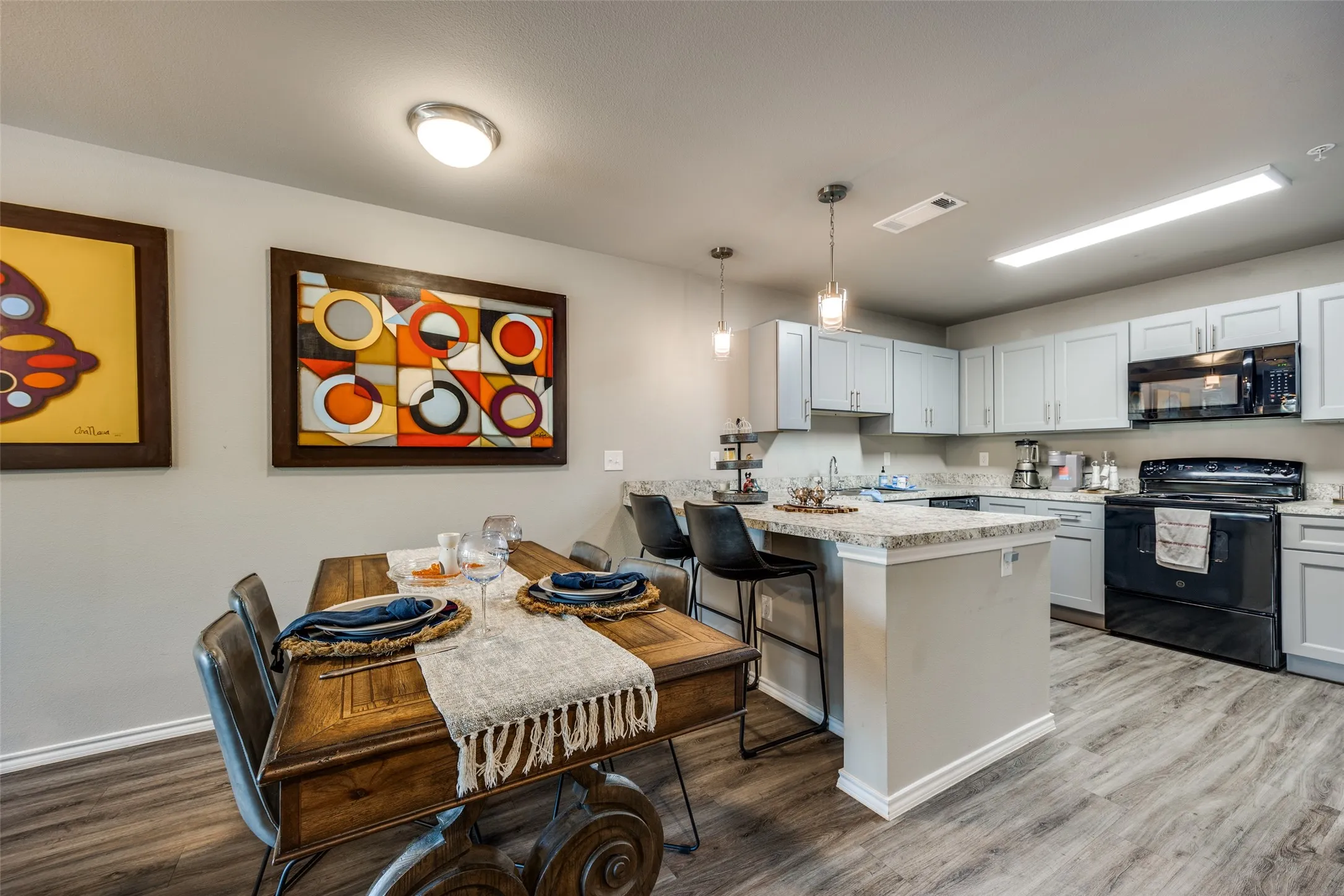 Kitchen featuring black appliances, a kitchen breakfast bar, a peninsula, light wood-type flooring, and hanging light fixtures
