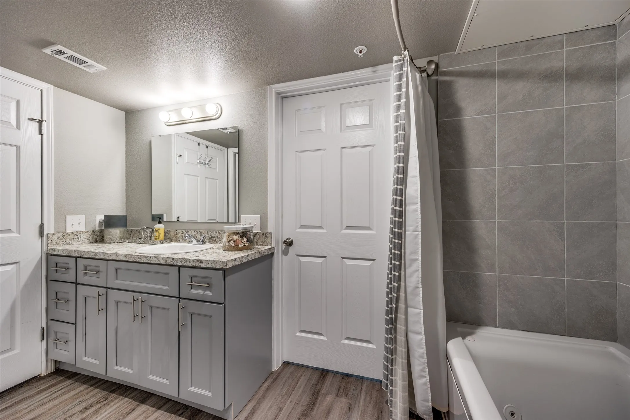 Bathroom with a textured ceiling, vanity, shower / tub combo, and light wood-type flooring