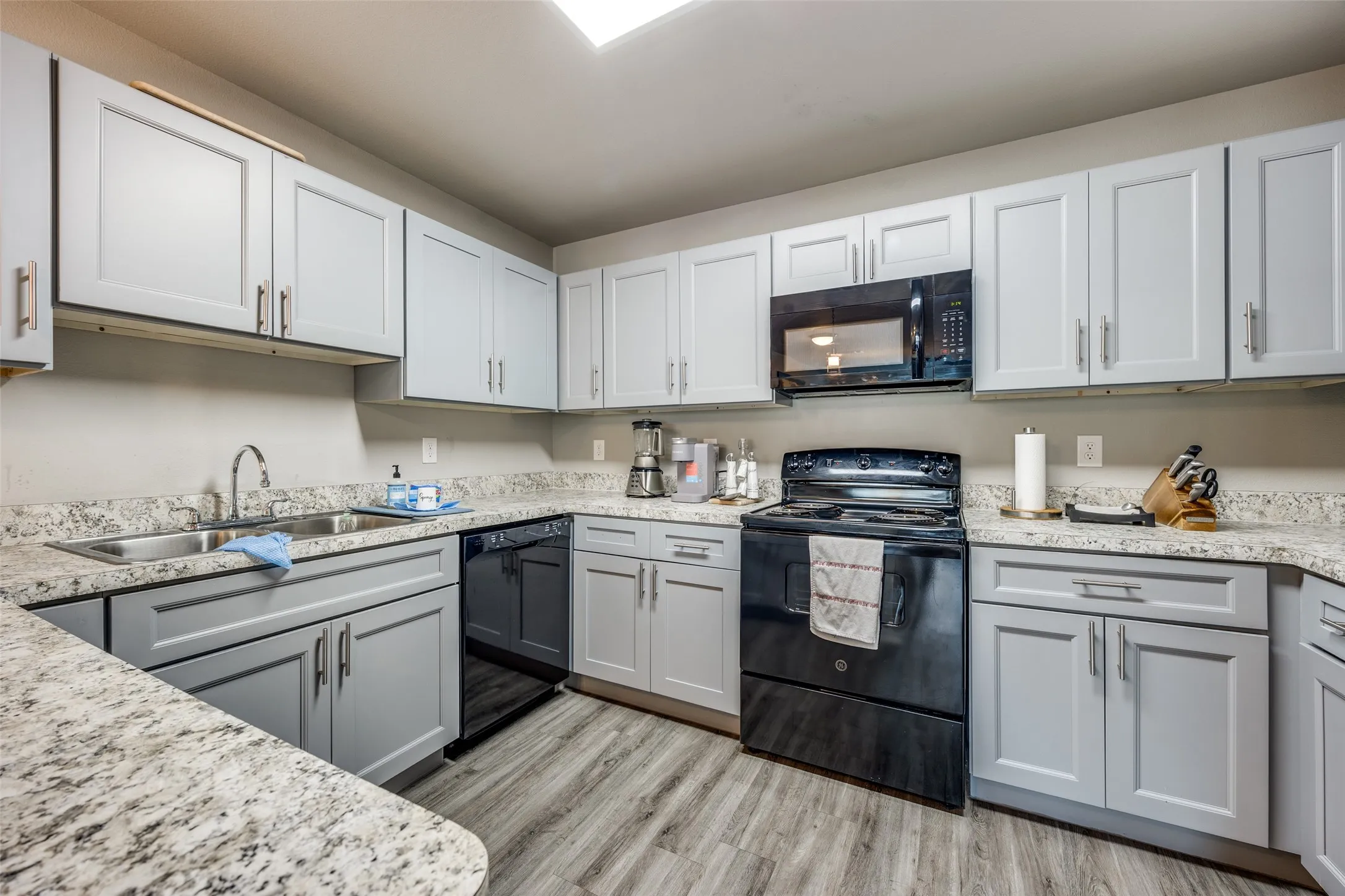 Kitchen with black appliances, light wood finished floors, and light stone countertops