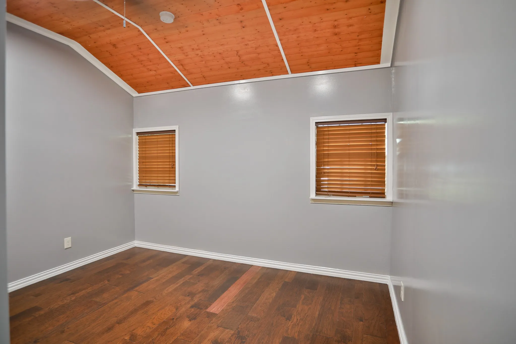 Room featuring a vaulted wood-paneled ceiling, two windows with horizontal blinds, gray painted walls, and wood-finish flooring