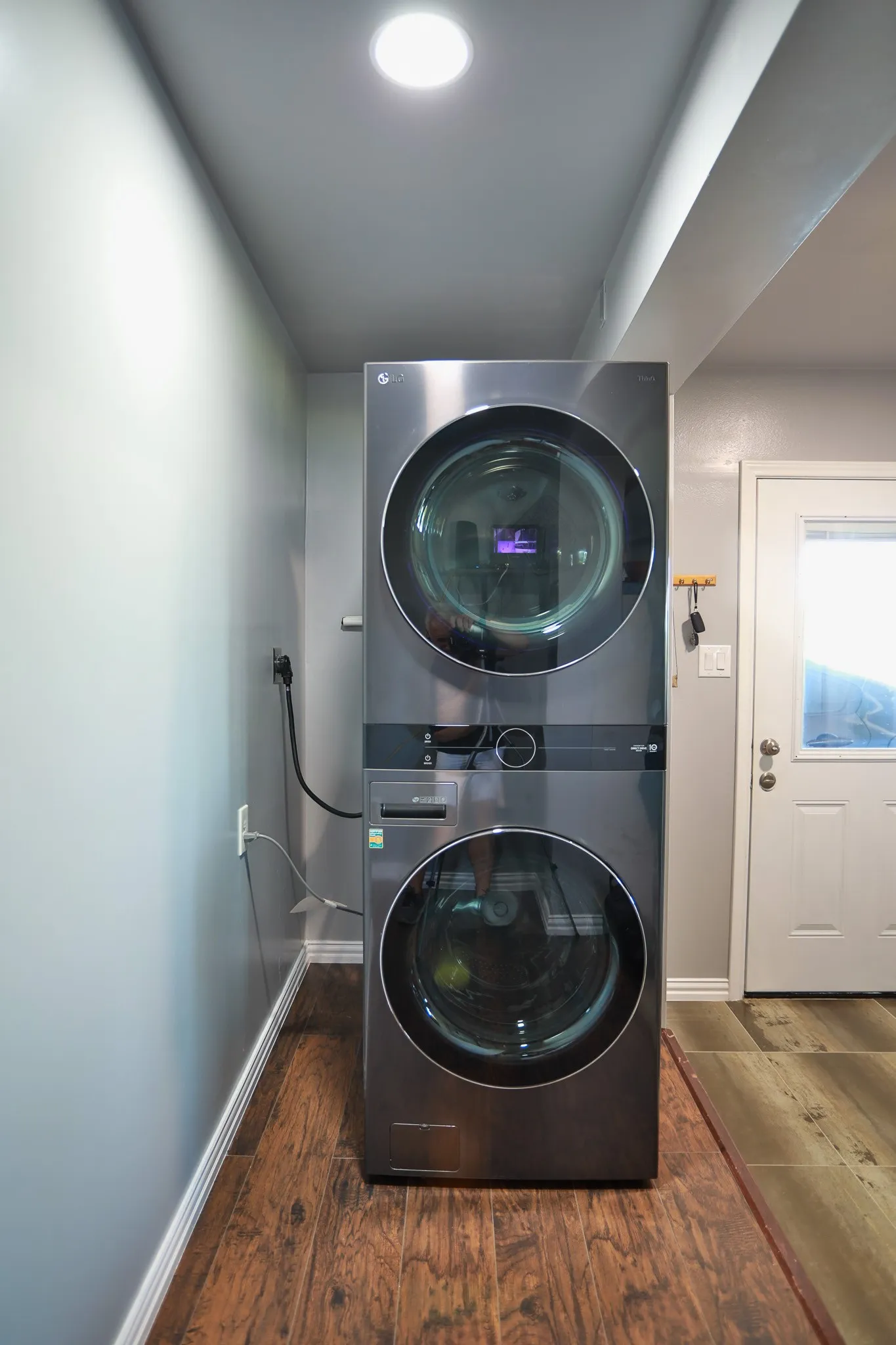 Dedicated laundry area featuring a stacked washer and dryer unit, recessed ceiling lighting, wood-finish flooring, and crisp white baseboards
