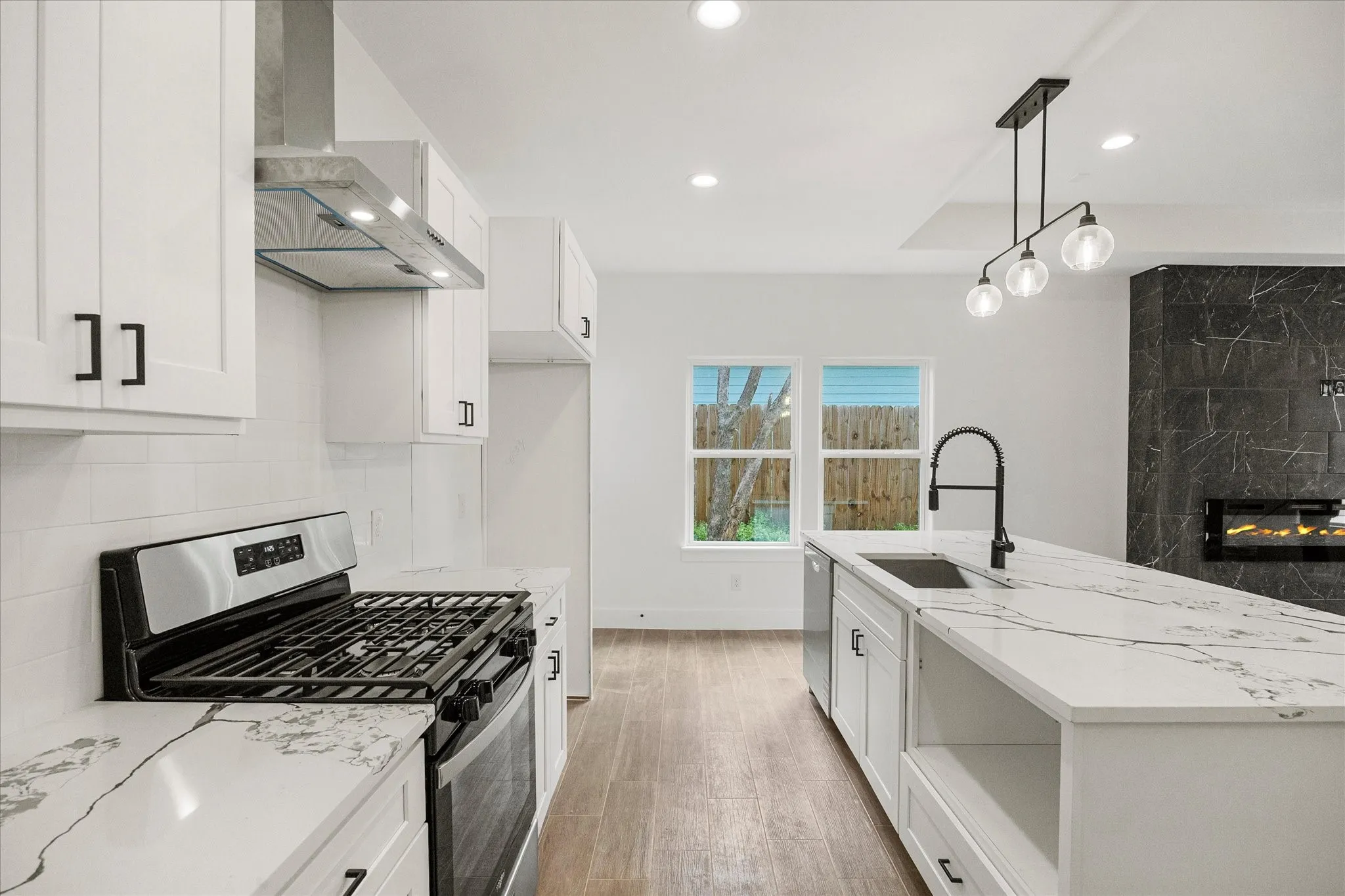 Kitchen featuring stainless steel appliances, white cabinetry, light stone counters, a kitchen island with sink, and a high end fireplace