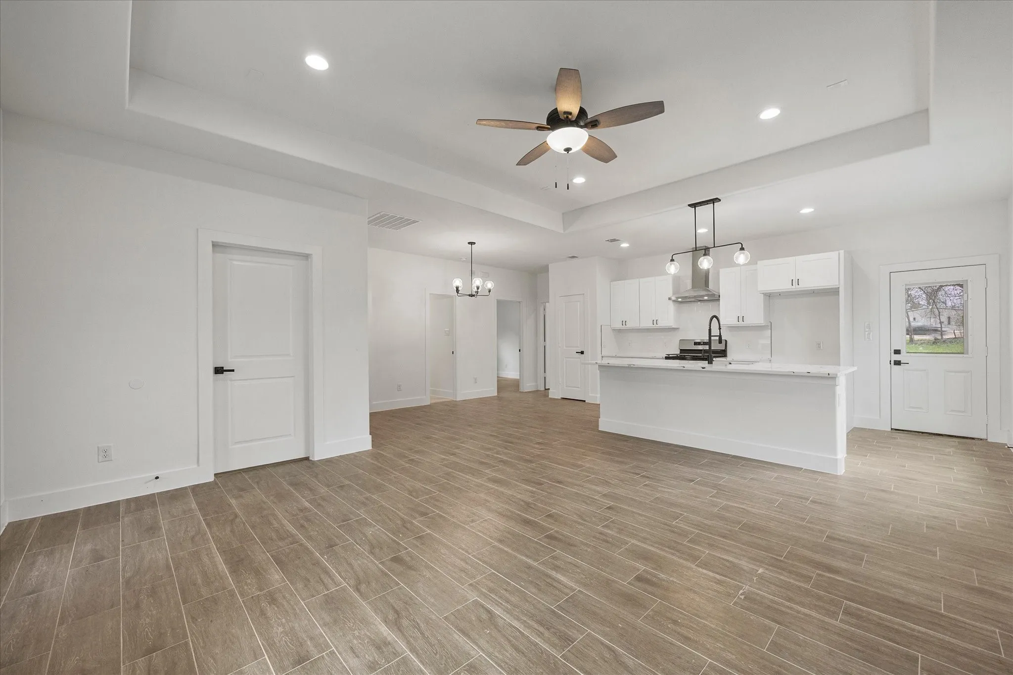 Unfurnished living room with a tray ceiling, a ceiling fan, suspended lighting, and wood finish floors