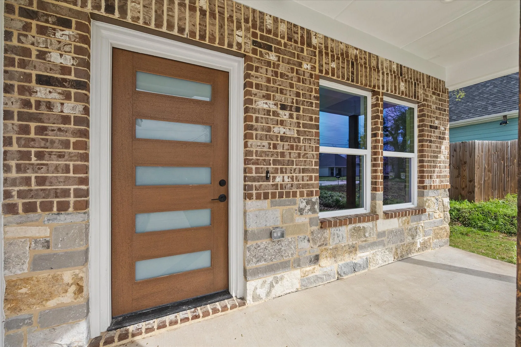 View of exterior entry with a porch, stone siding, and brick siding