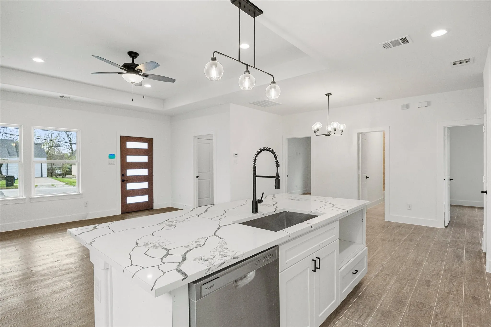 Kitchen featuring stainless steel dishwasher, a raised ceiling, a center island with sink, open floor plan, and white​​‌​​​​‌​​‌‌​‌‌​​​‌‌​‌​‌​‌​​​‌​​ cabinetry