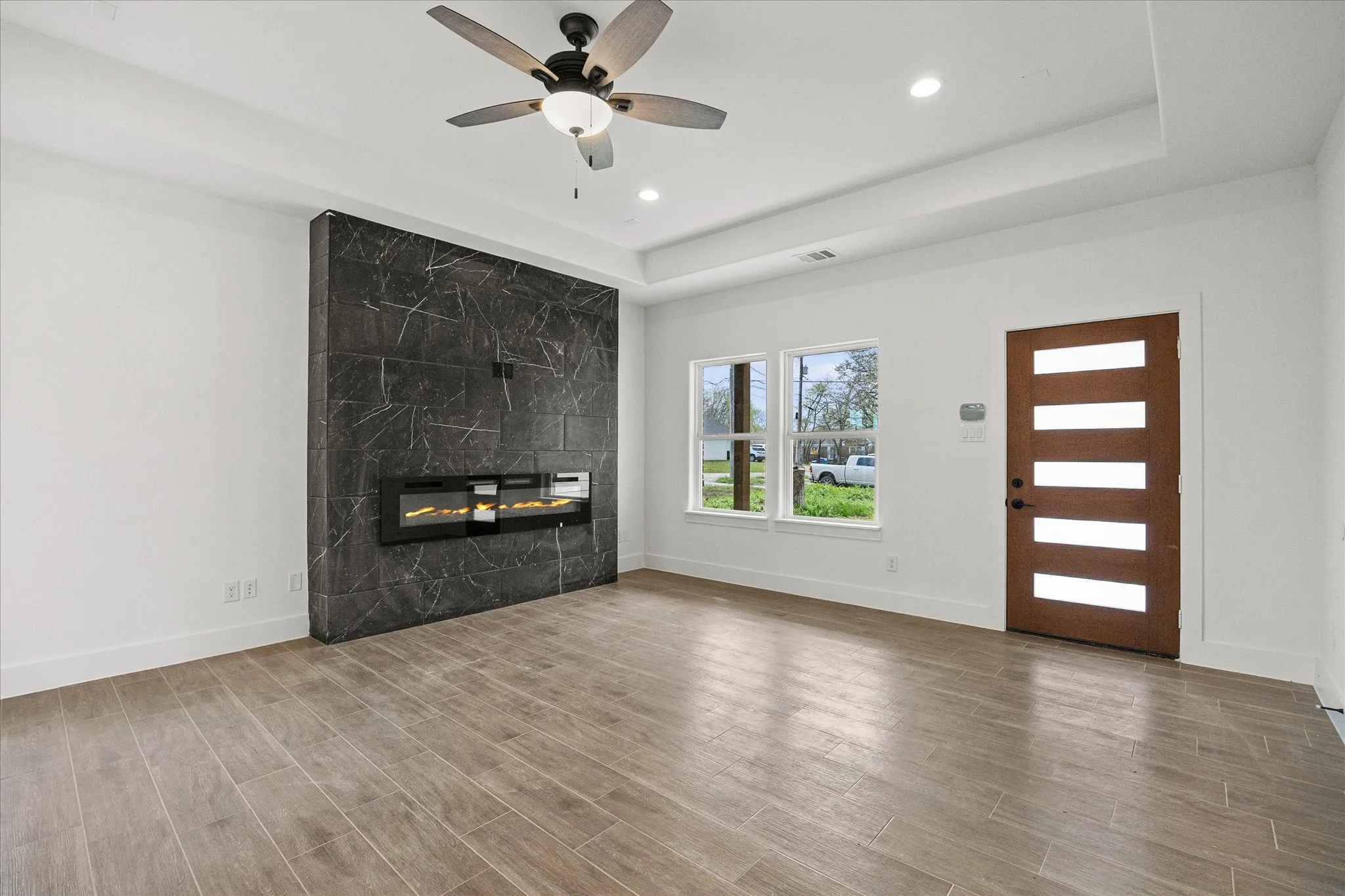 Unfurnished living room with wood tiled floors, a ceiling fan, a premium fireplace, recessed lighting, and a tray ceiling