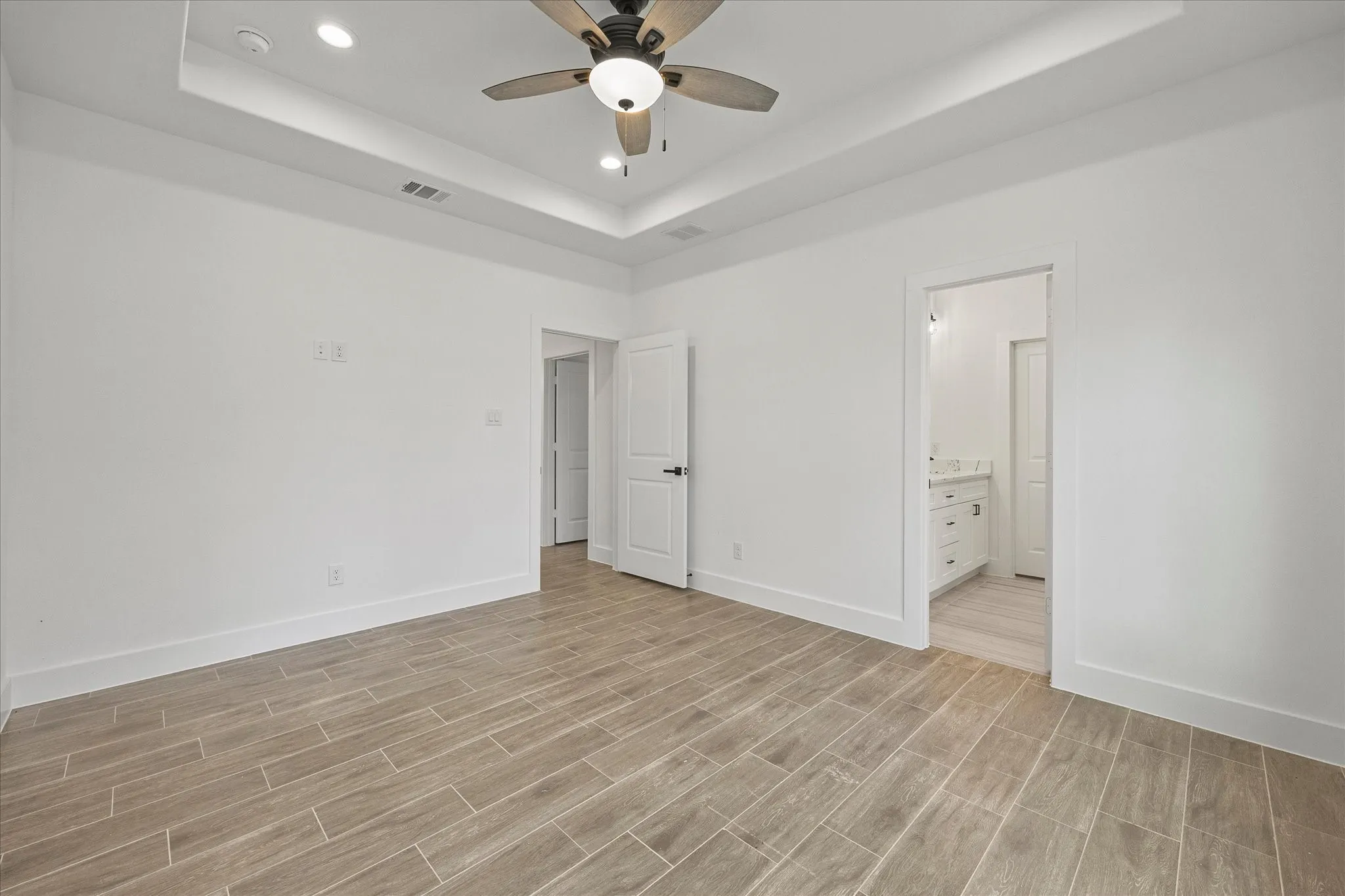 Unfurnished bedroom with recessed lighting, wood tiled floors, a ceiling fan, a tray ceiling, and ensuite bath