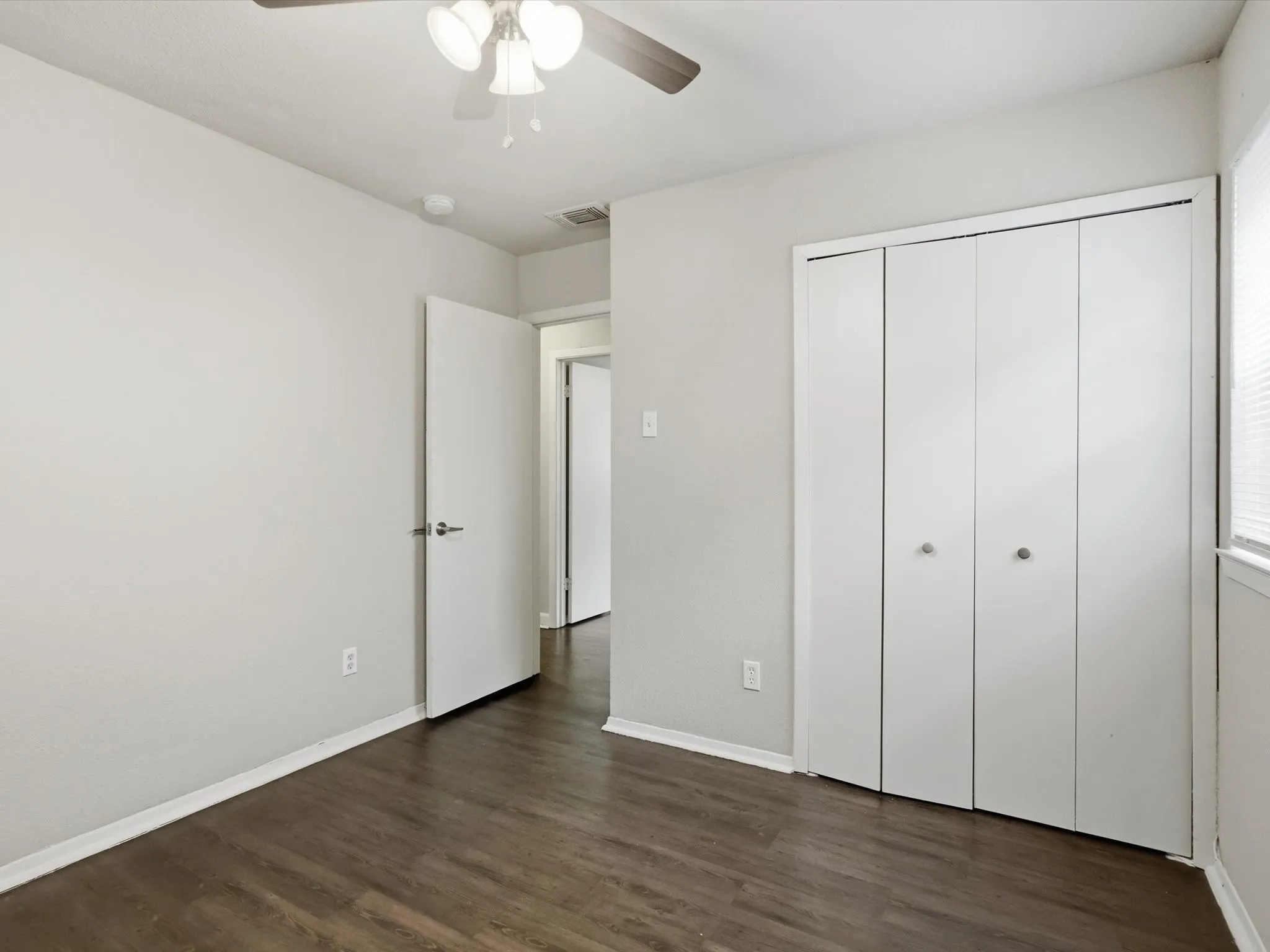 Primary bedroom looking towards white bi-fold closet and hallway.