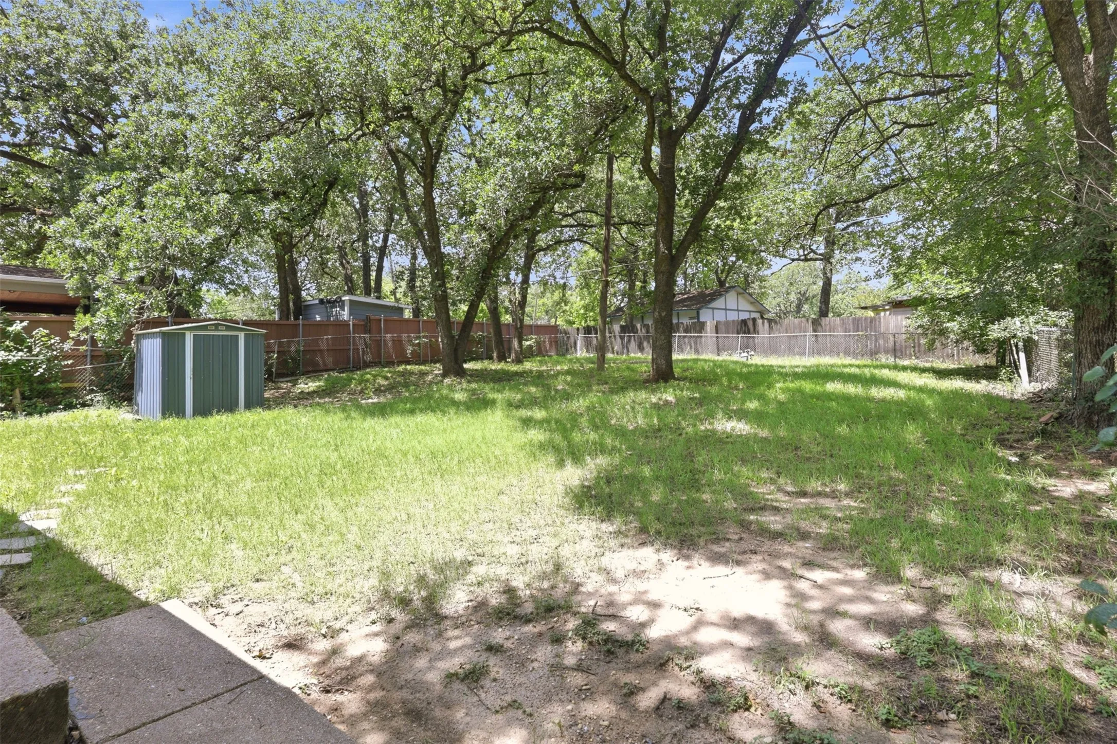 Spacious backyard with a vibrant green lawn, mature trees providing ample shade, and a privacy fence.