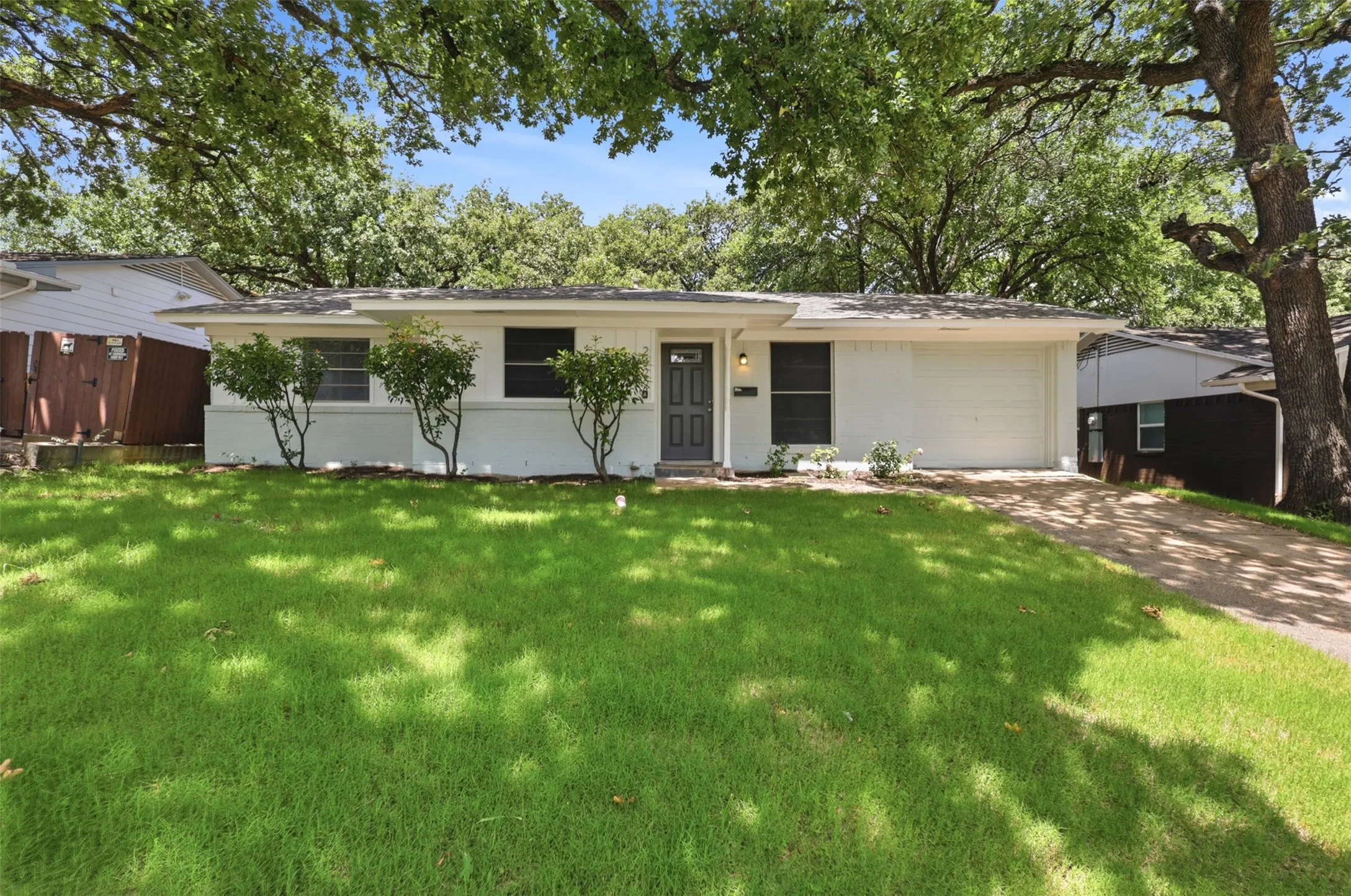 Single-story residence featuring a two-tone painted exterior, an attached garage with a white door, a concrete driveway, and established front landscaping.