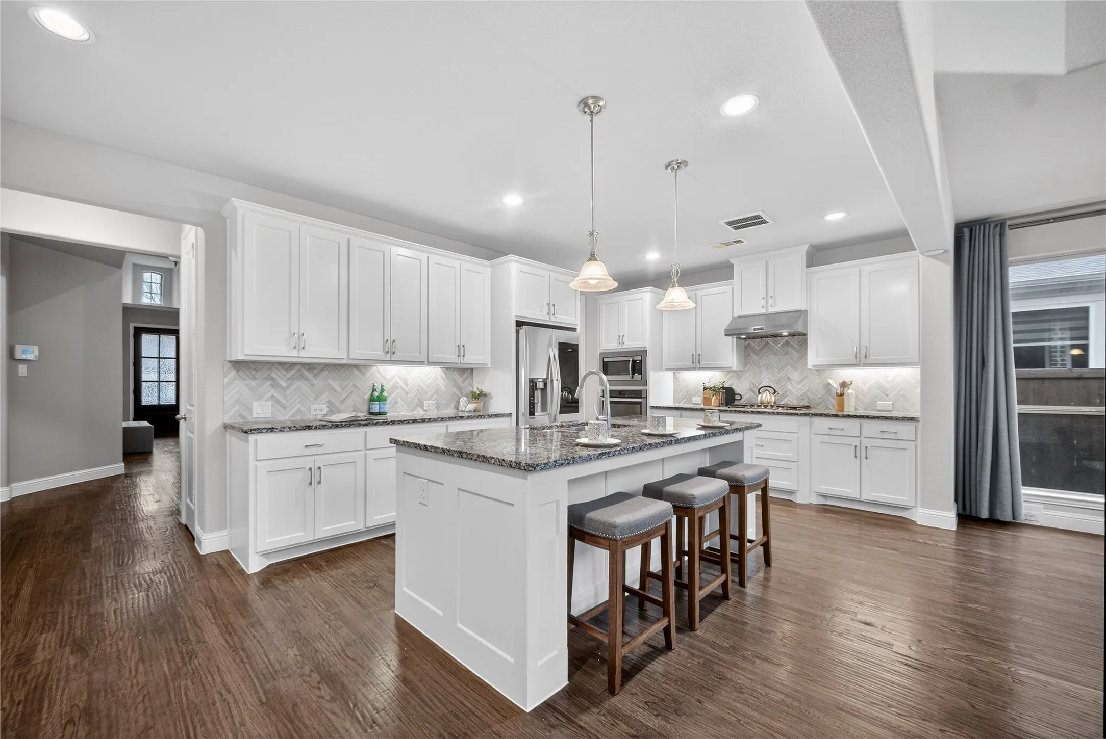 Kitchen with a kitchen bar, dark wood-type flooring, white cabinetry, and an island with sink