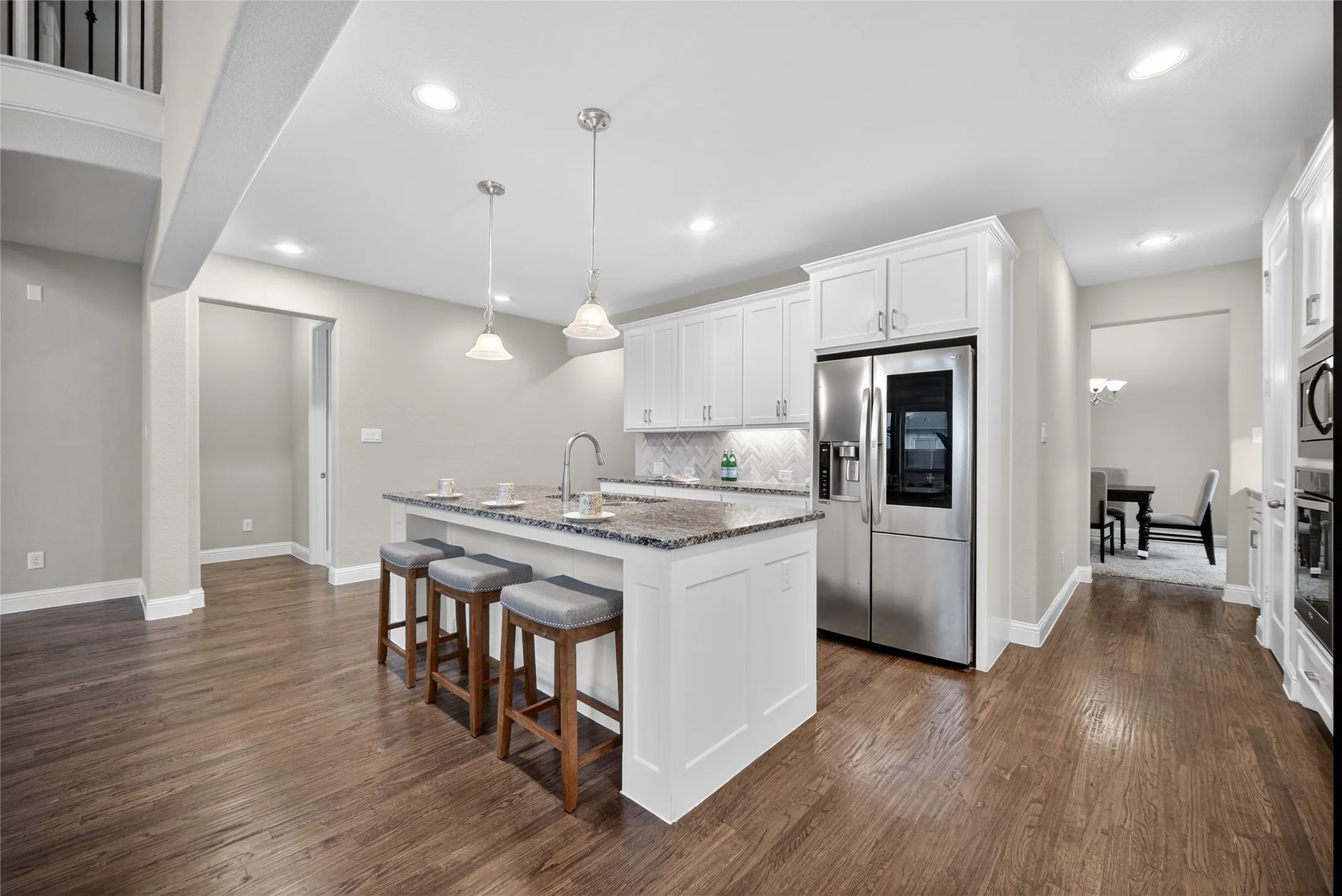 Kitchen with stainless steel appliances, white cabinets, dark wood-style floors, a kitchen island with sink, and a kitchen bar