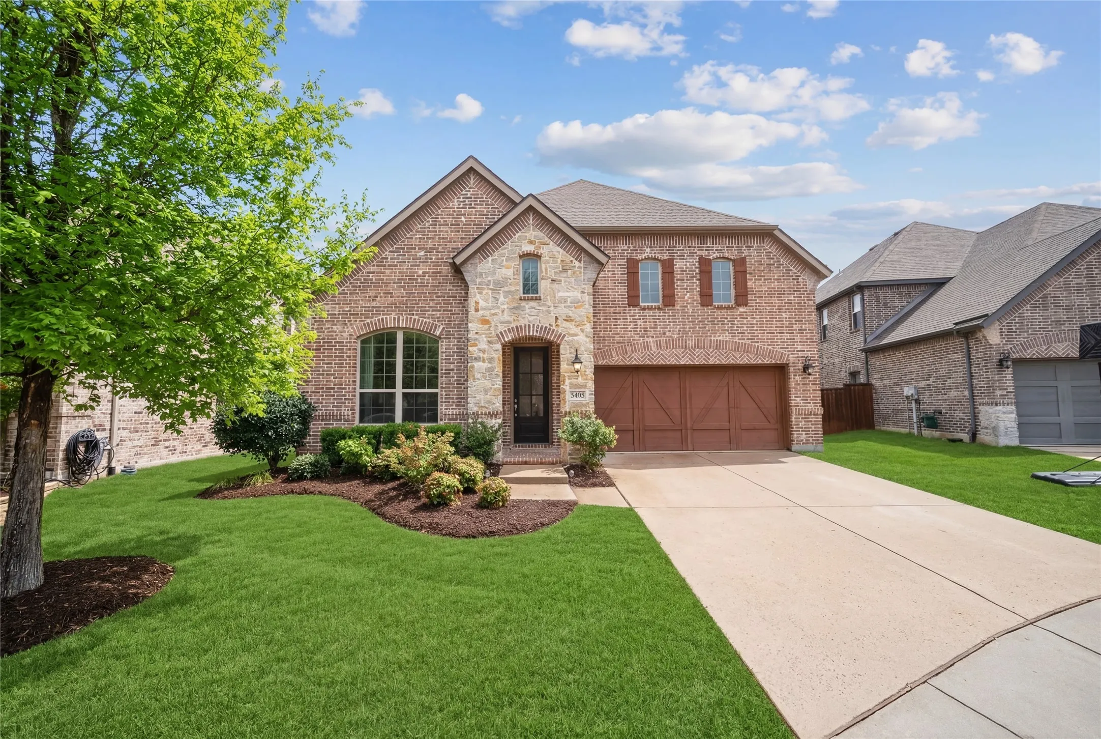 French country inspired facade featuring brick siding, concrete driveway, and an attached garage