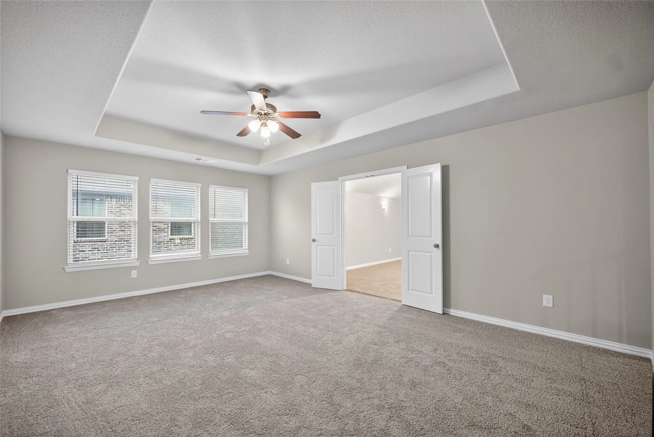 Unfurnished bedroom with carpet, a raised ceiling, a ceiling fan, and a textured ceiling