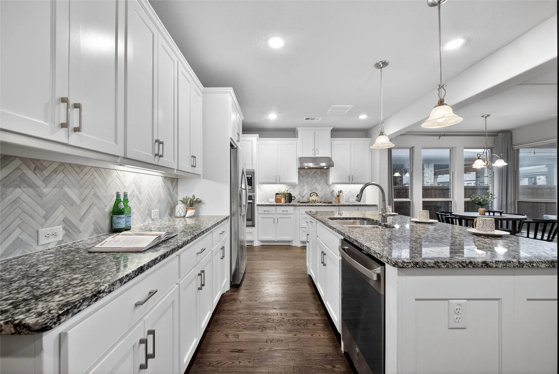 Kitchen featuring dark stone counters, dark wood-style flooring, white cabinets, stainless steel appliances, and an island with sink