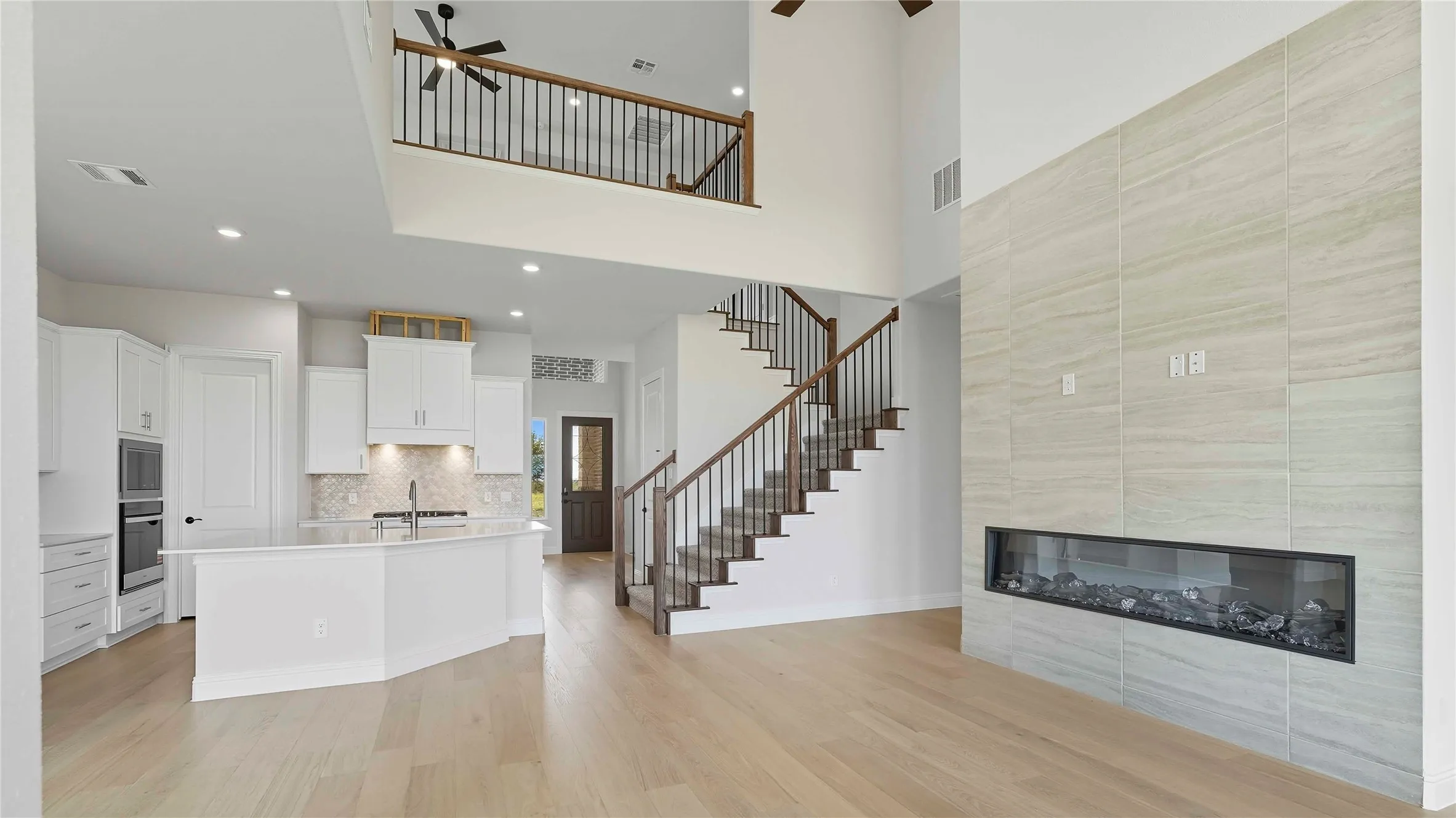 Kitchen with a tile fireplace, a ceiling fan, white cabinetry, a center island with sink, and light wood finished floors