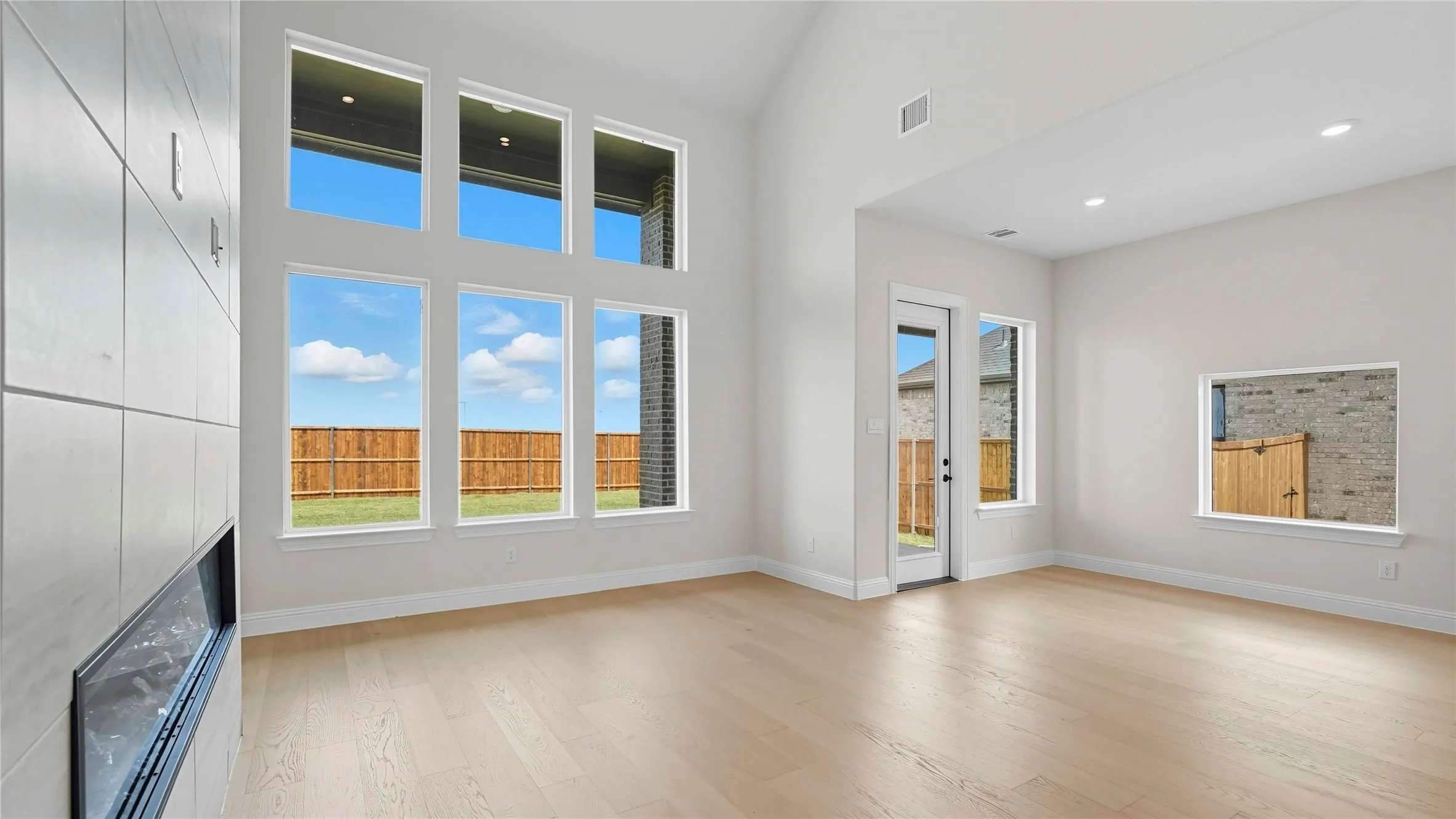 Unfurnished living room featuring a high ceiling, light wood finished floors, a tiled fireplace, and recessed lighting