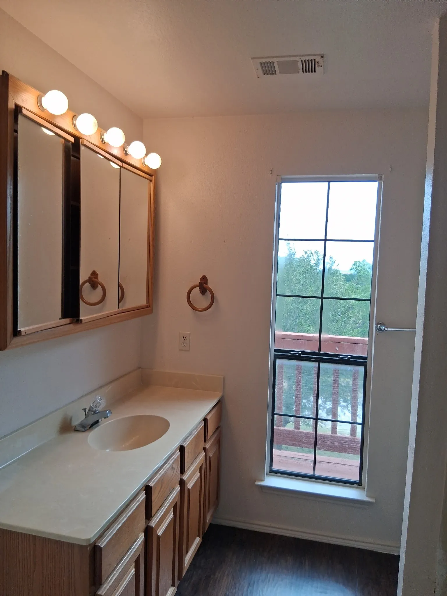 Bathroom featuring a wood-finish vanity with an integrated sink and light-toned countertop, a multi-bulb vanity light fixture, and a gridded window