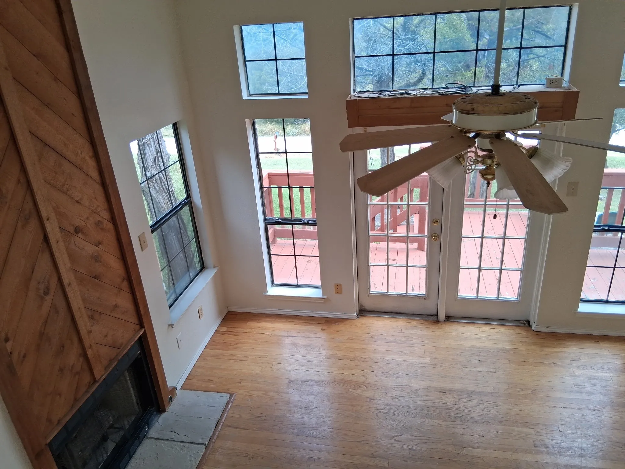 Spacious room featuring light wood-finish flooring, a fireplace with a stone hearth and wood-paneled surround, and multiple windows