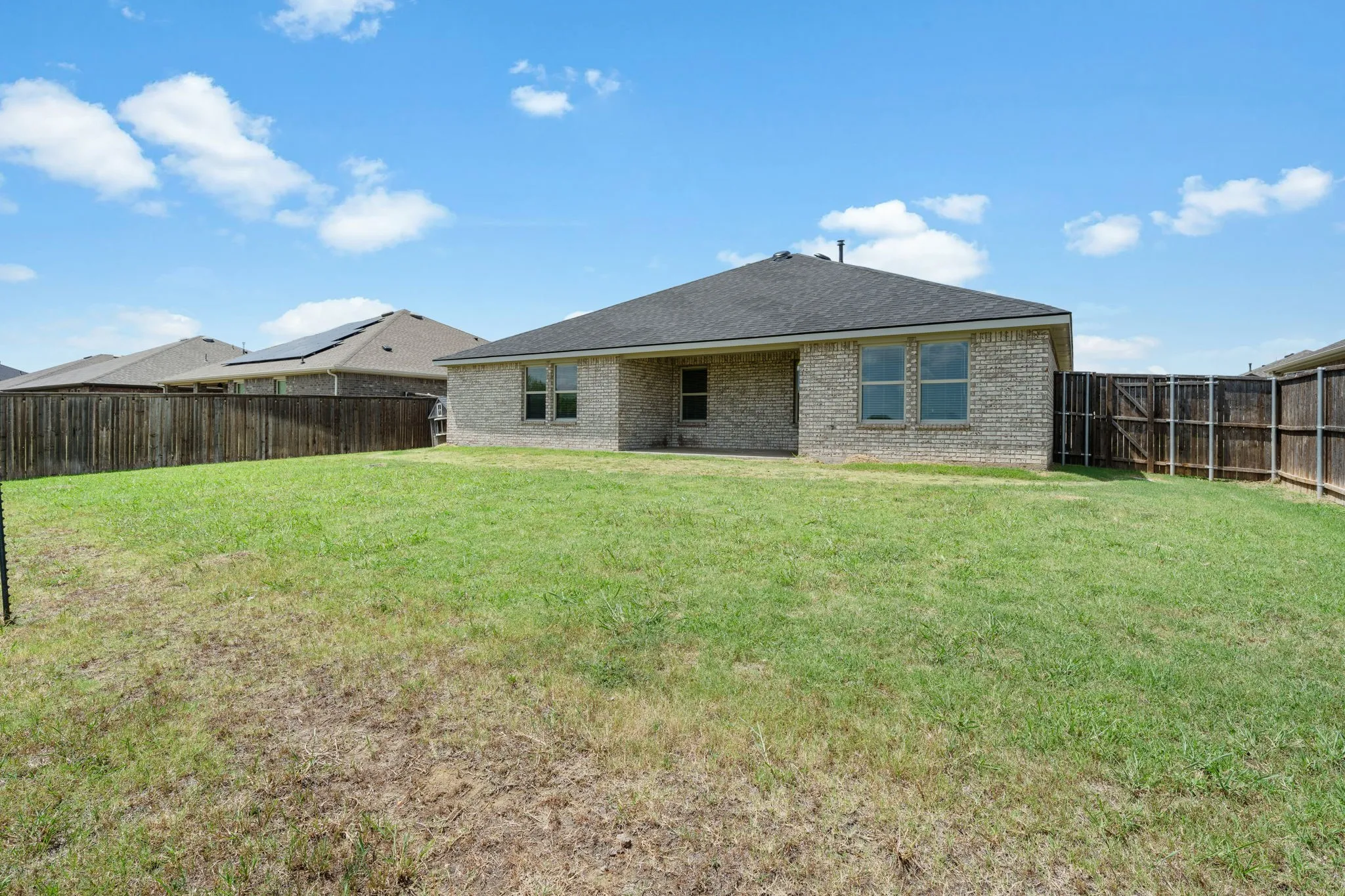 Expansive backyard featuring a manicured lawn, full privacy fencing, brick exterior, dark shingle roofing, and multiple rear-facing windows