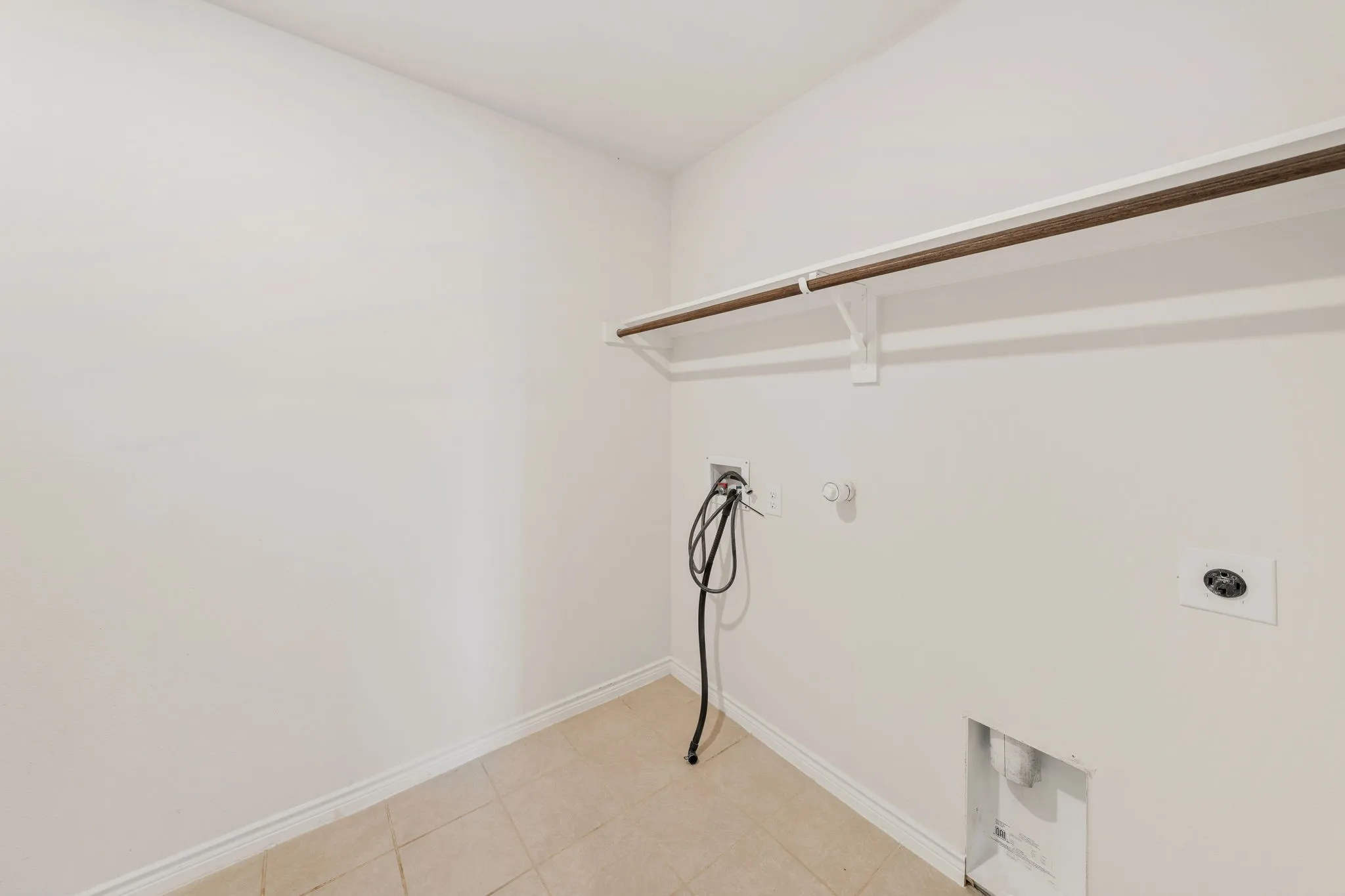 Laundry utility area featuring tiled flooring, a built-in shelf, and a clothing rod