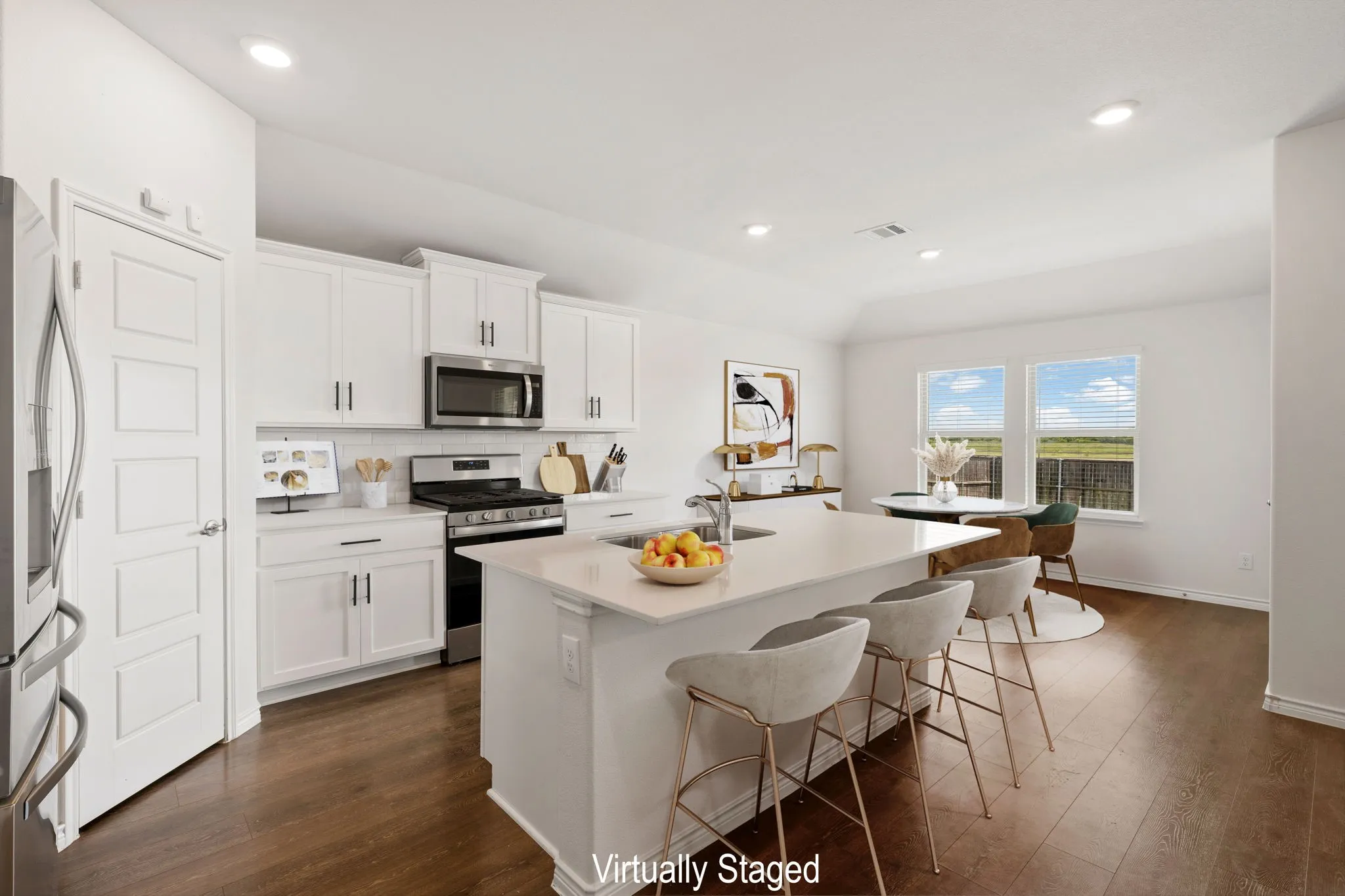 Kitchen featuring a large central island with seating, white shaker-style cabinetry, stainless steel appliances, wood-finish flooring, and recessed lighting