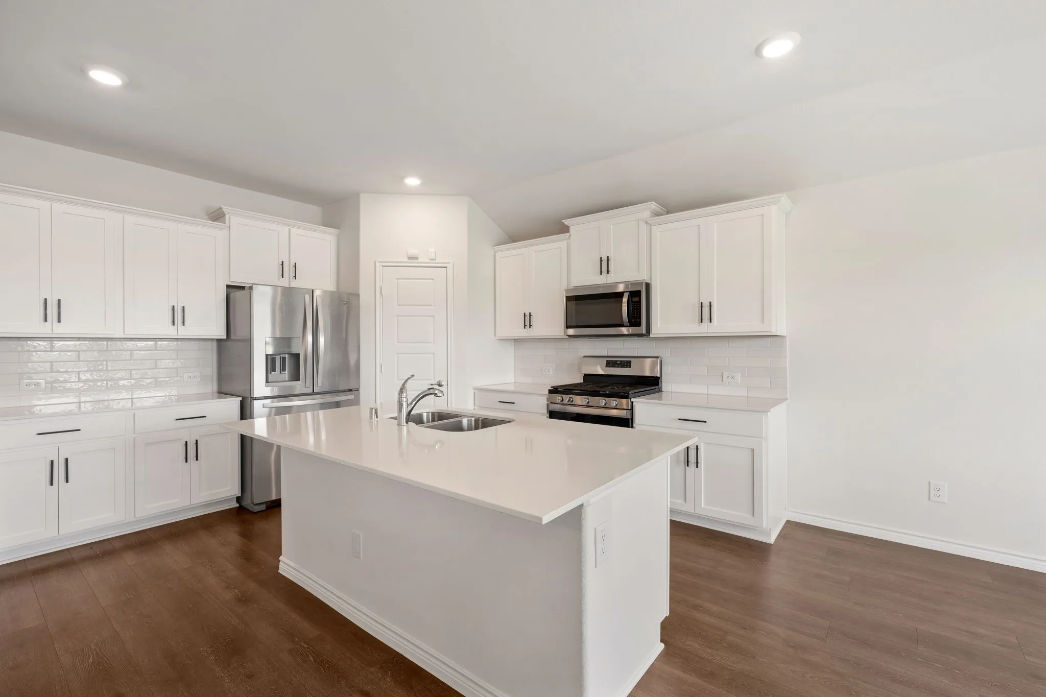 Open-concept kitchen featuring an island with an undermount sink, white cabinetry, a subway tile backsplash, stainless steel appliances, and wood-finish flooring