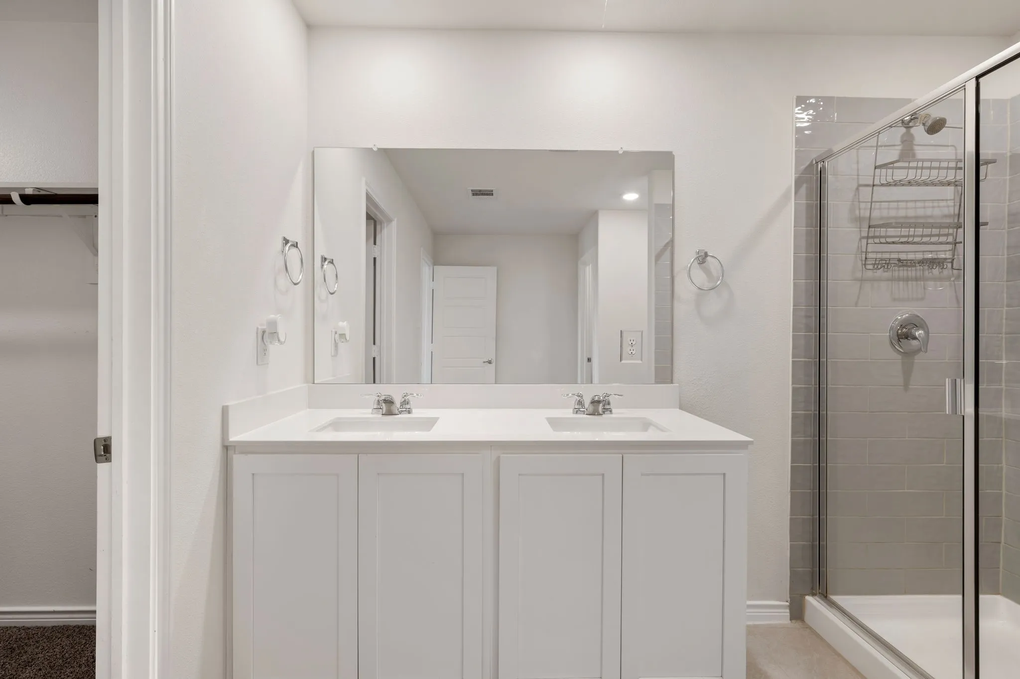 Bathroom featuring a dual vanity with white cabinetry and integrated sinks, a large wall-mounted mirror, and a glass-enclosed shower with subway tile surround