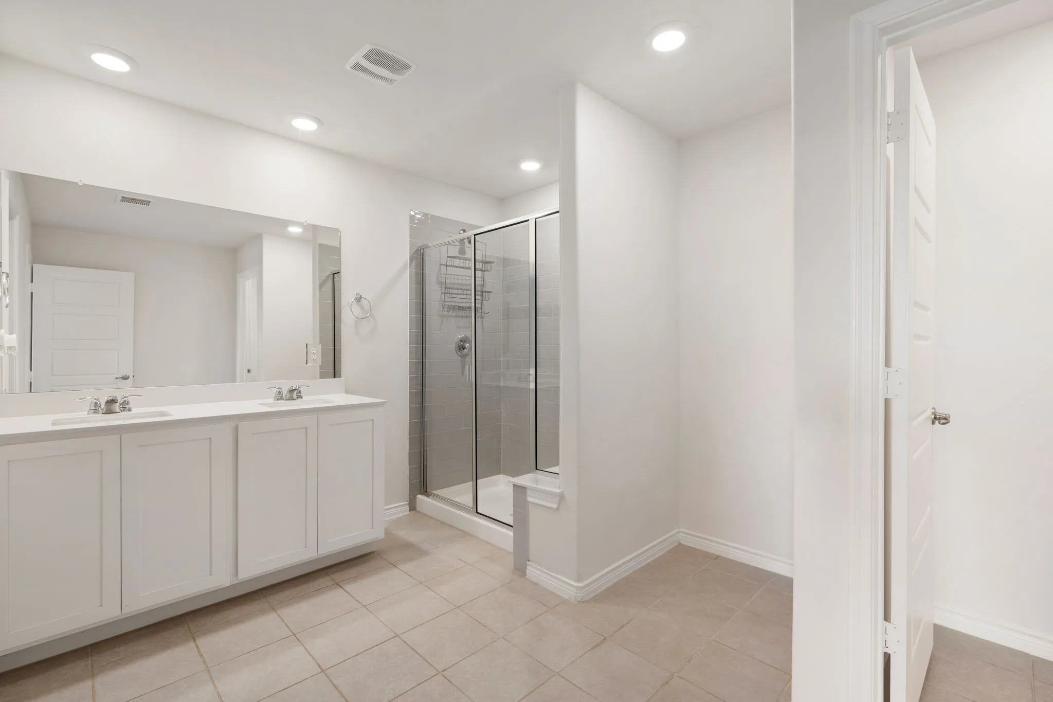 Bathroom featuring a dual vanity with white cabinetry, a large frameless mirror, and a glass-enclosed shower with subway tile surround