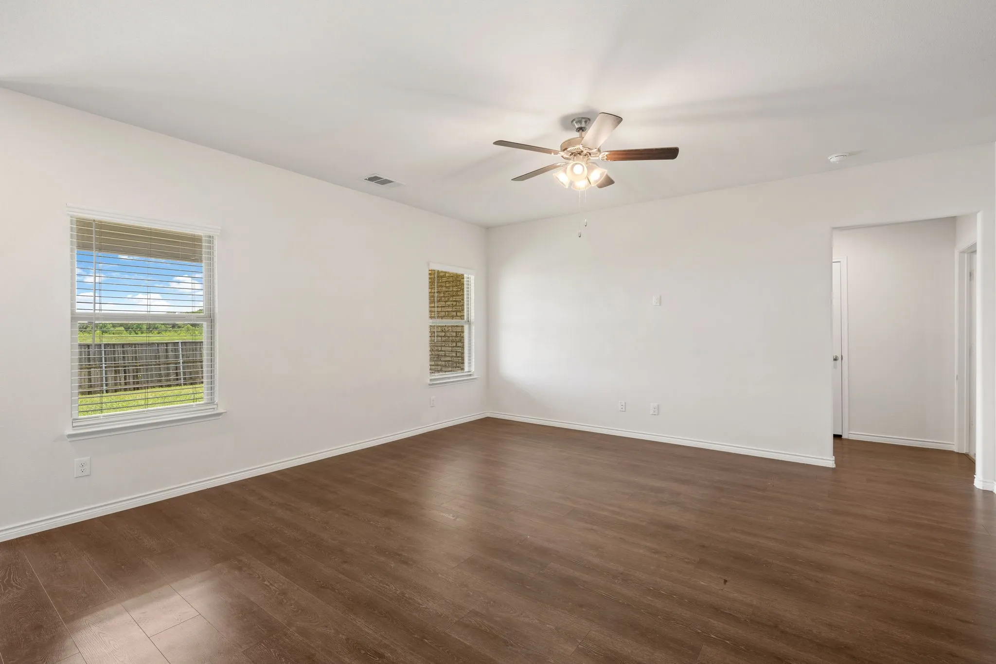Spacious interior room featuring wood-finish flooring, white walls, and a ceiling fan with integrated lighting