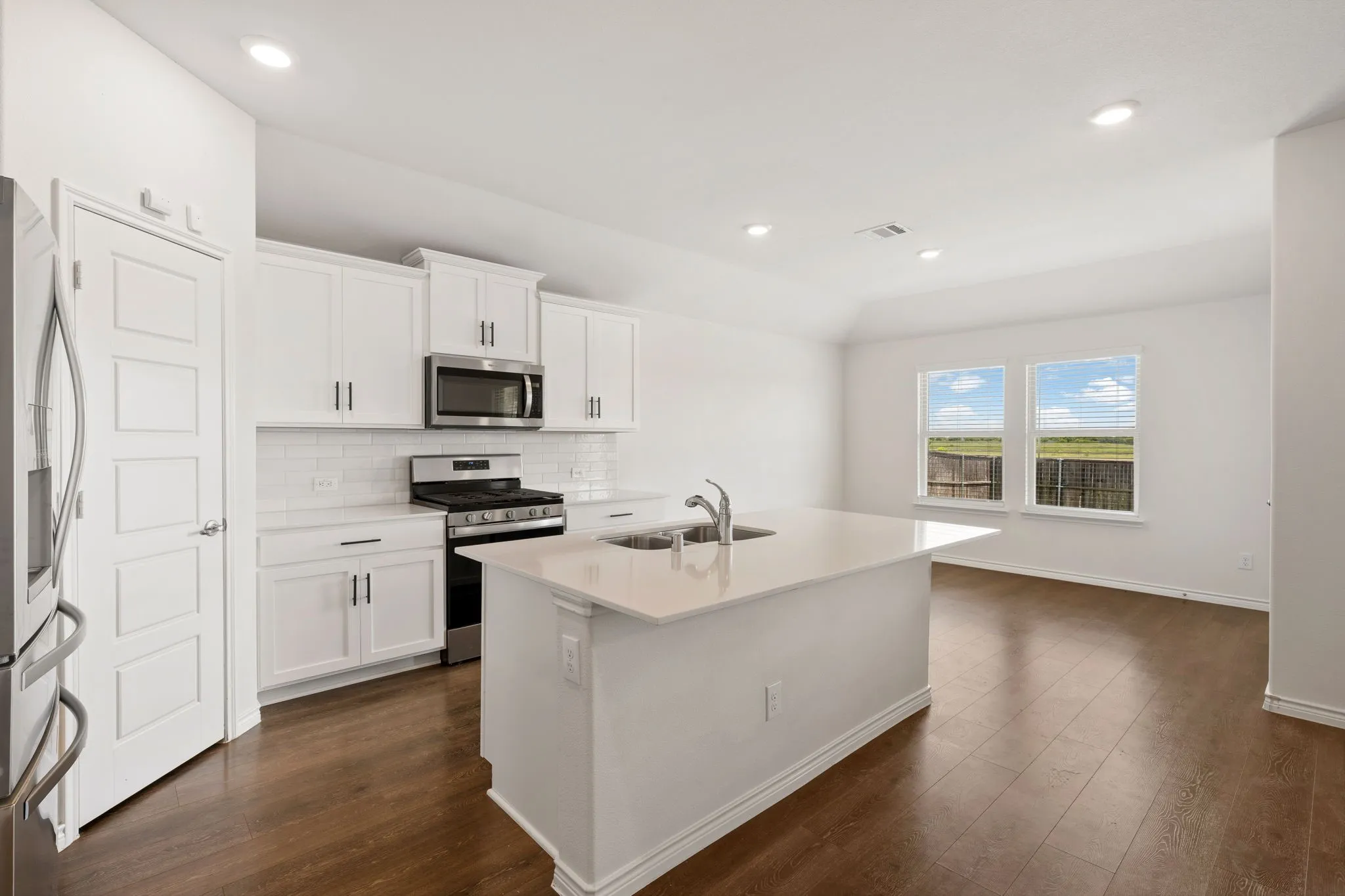 Modern kitchen featuring an island with a stainless steel sink, white cabinetry with dark hardware, stainless steel appliances, and a white subway tile backsplash