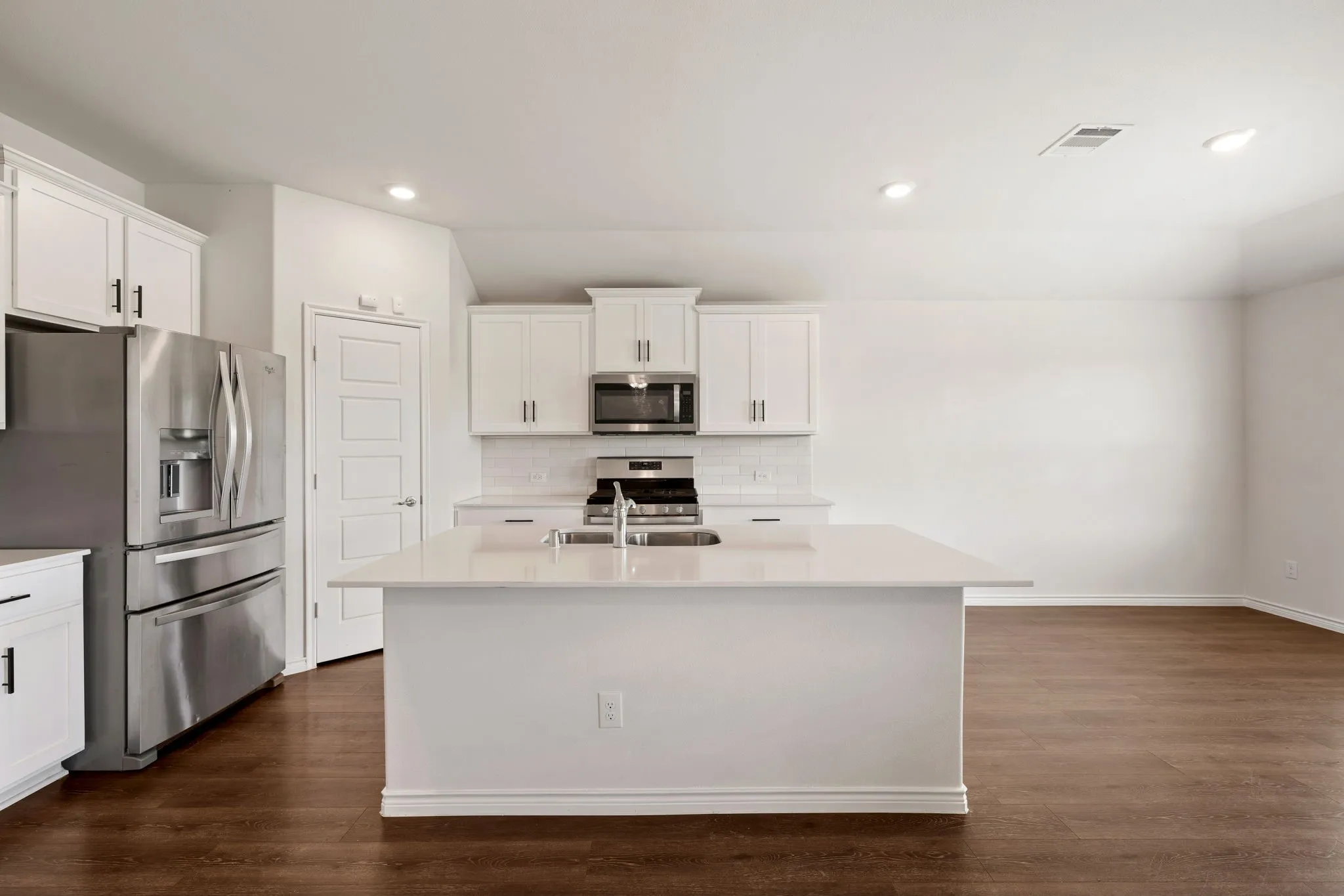 Kitchen featuring a central island with an undermount sink, white cabinetry with dark hardware, stainless steel appliances, and wood-finish flooring
