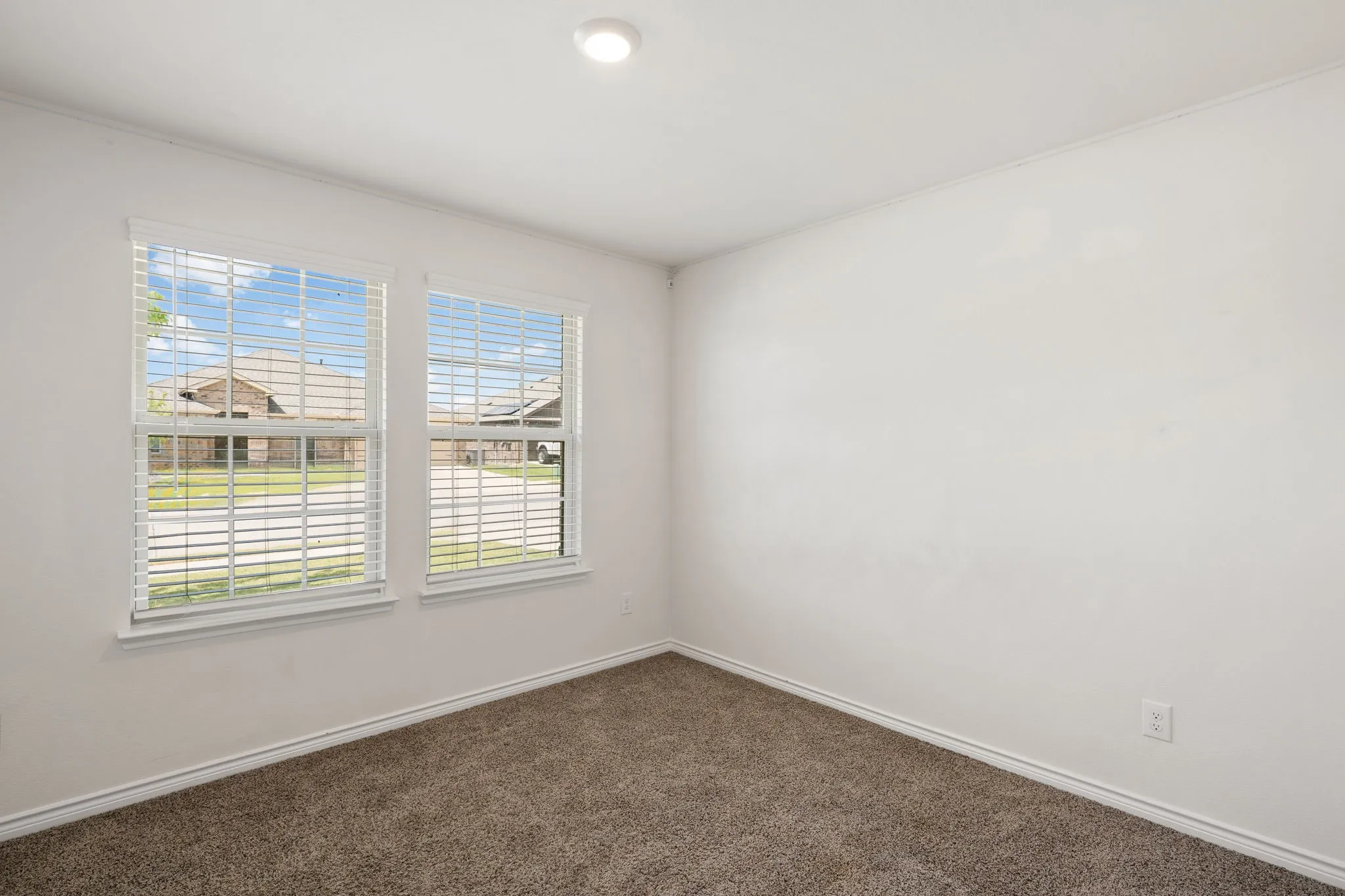 Carpeted room with two double-hung windows, white blinds, and white trim
