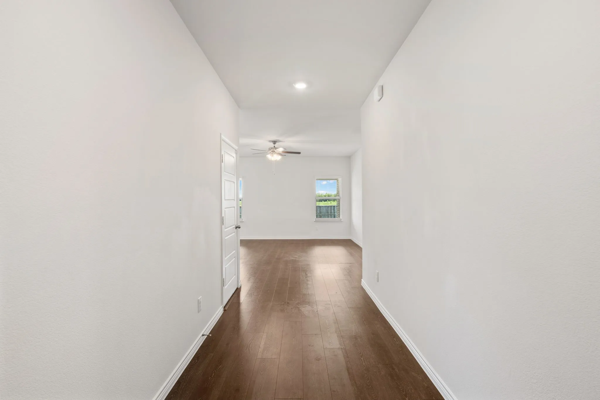 Hallway with wood-finish flooring, white walls, recessed lighting, and a white interior door