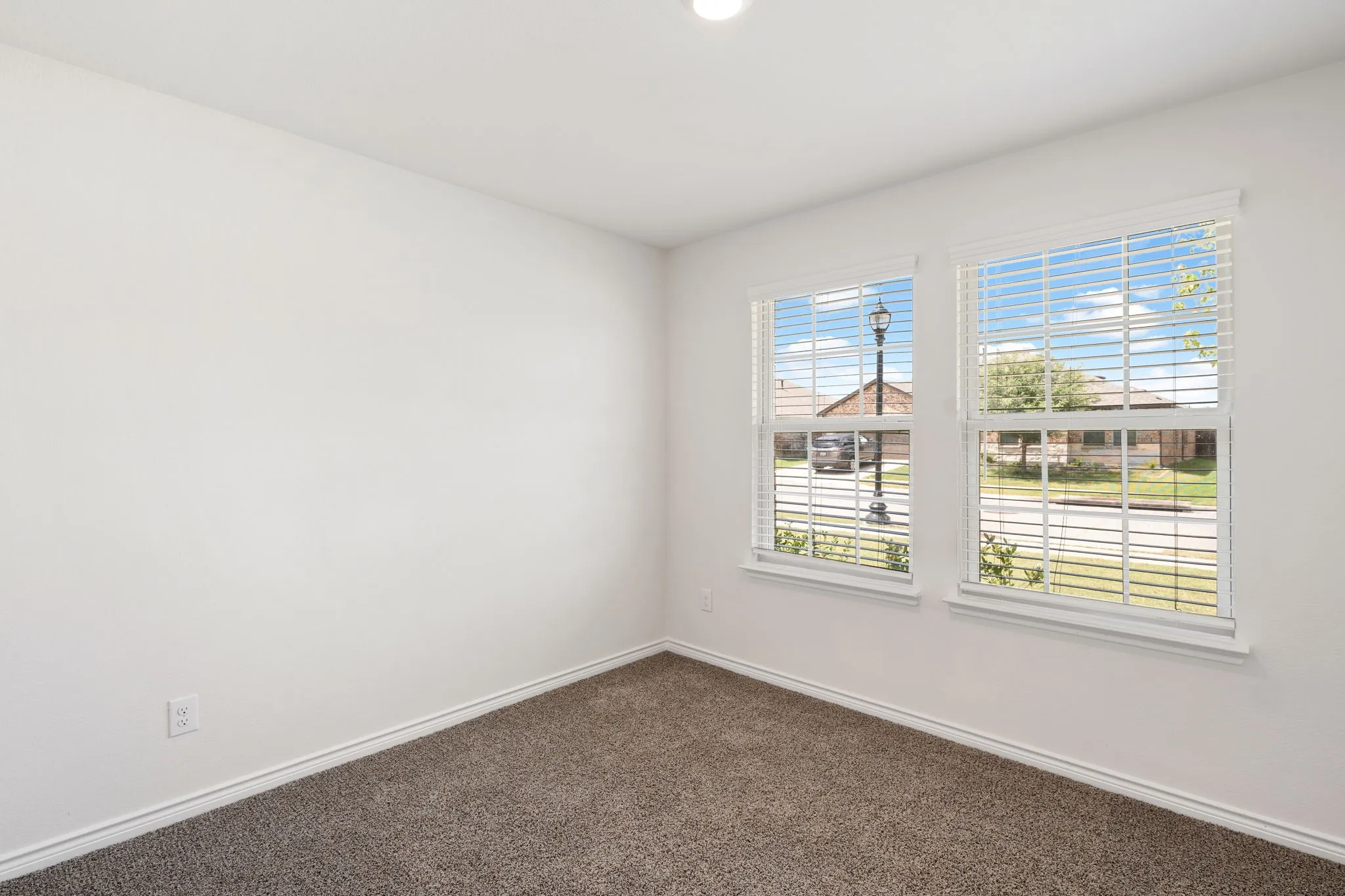 Room featuring two windows with white horizontal blinds, white walls, and dark gray carpet flooring
