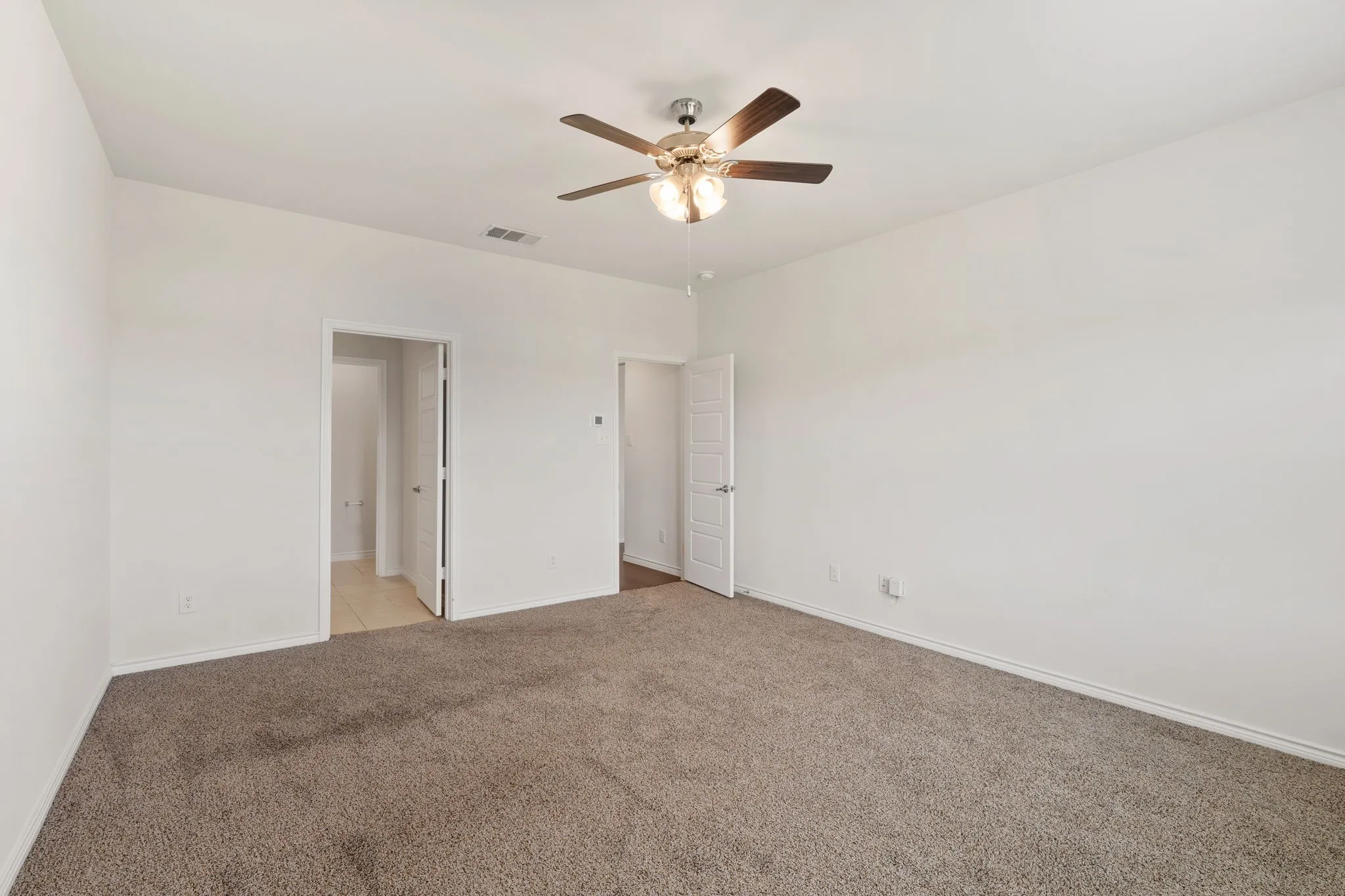 Spacious room featuring neutral carpeting, light-colored walls, and a ceiling fan with integrated lighting