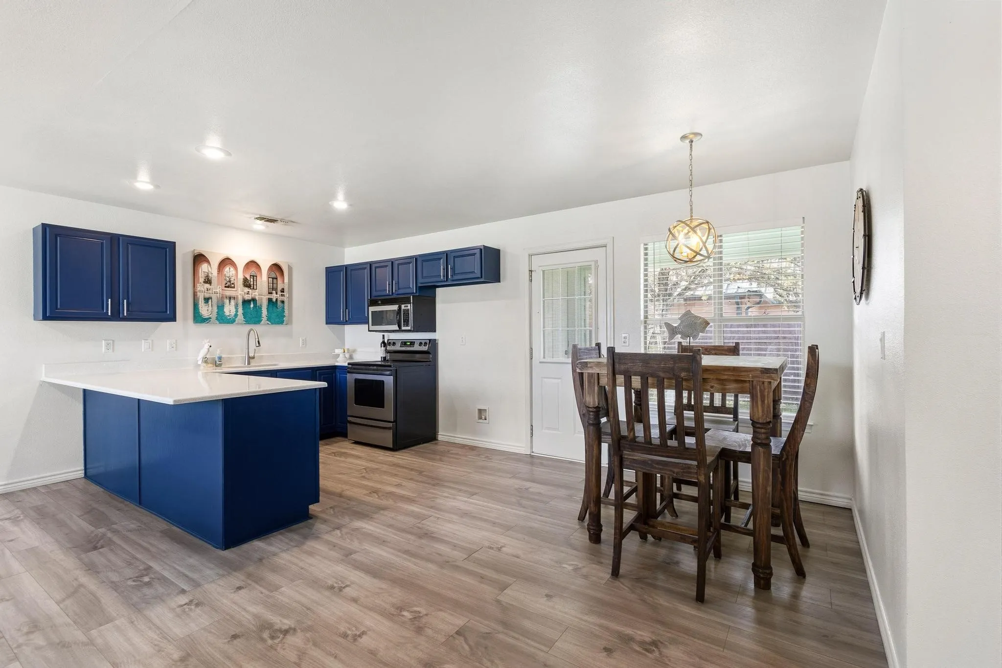 Kitchen featuring blue cabinetry, a peninsula, light countertops, stainless steel appliances, and pendant lighting