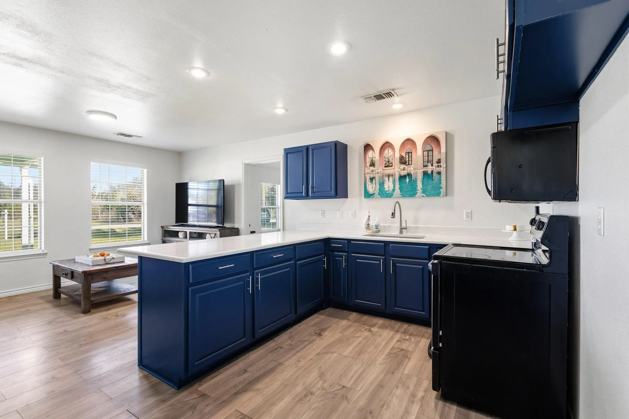 Kitchen featuring blue cabinets, a peninsula, black appliances, light wood-type flooring, and recessed lighting