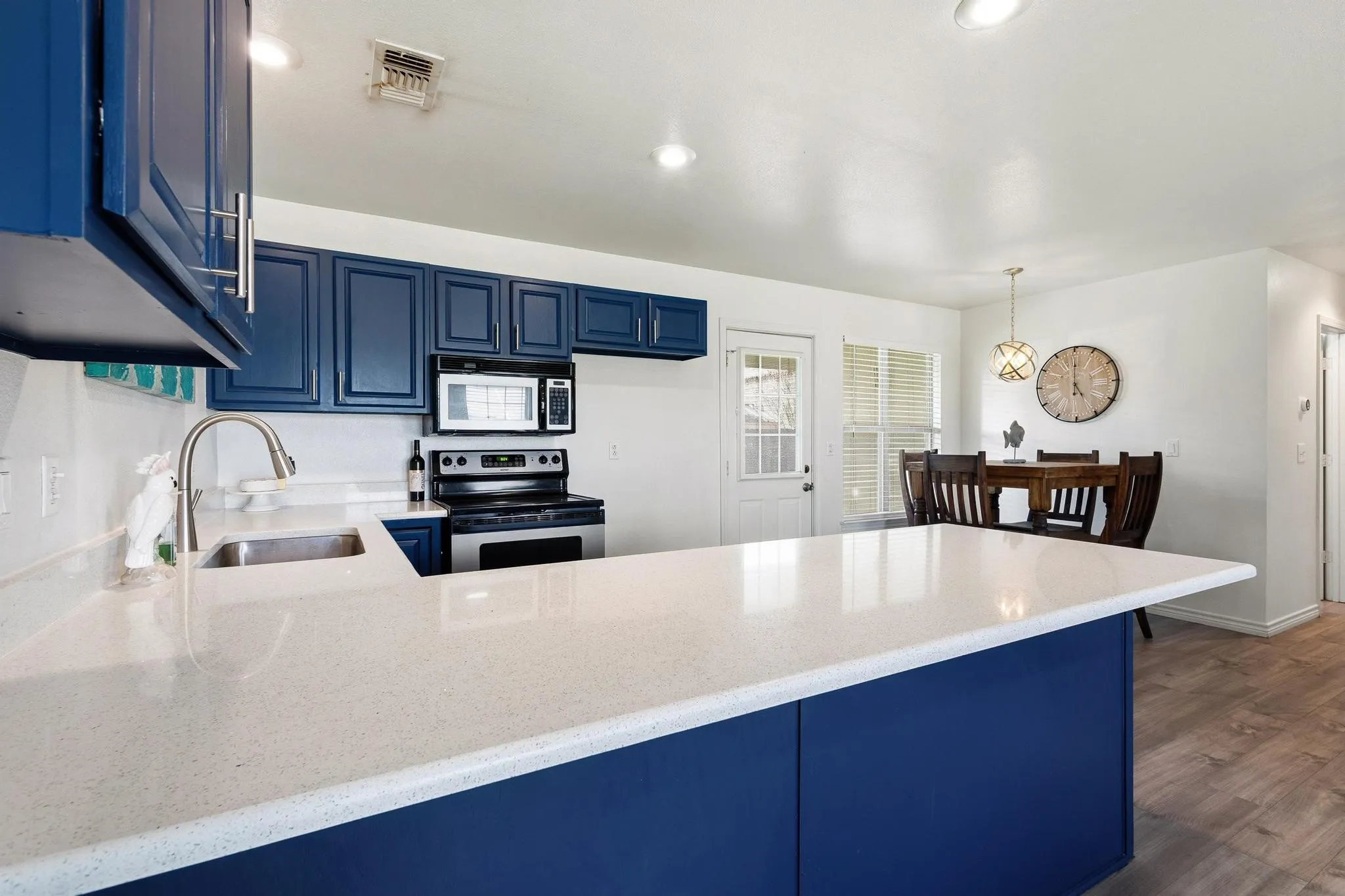 Kitchen featuring blue cabinetry, electric range, a peninsula, dark wood-type flooring, and light stone countertops