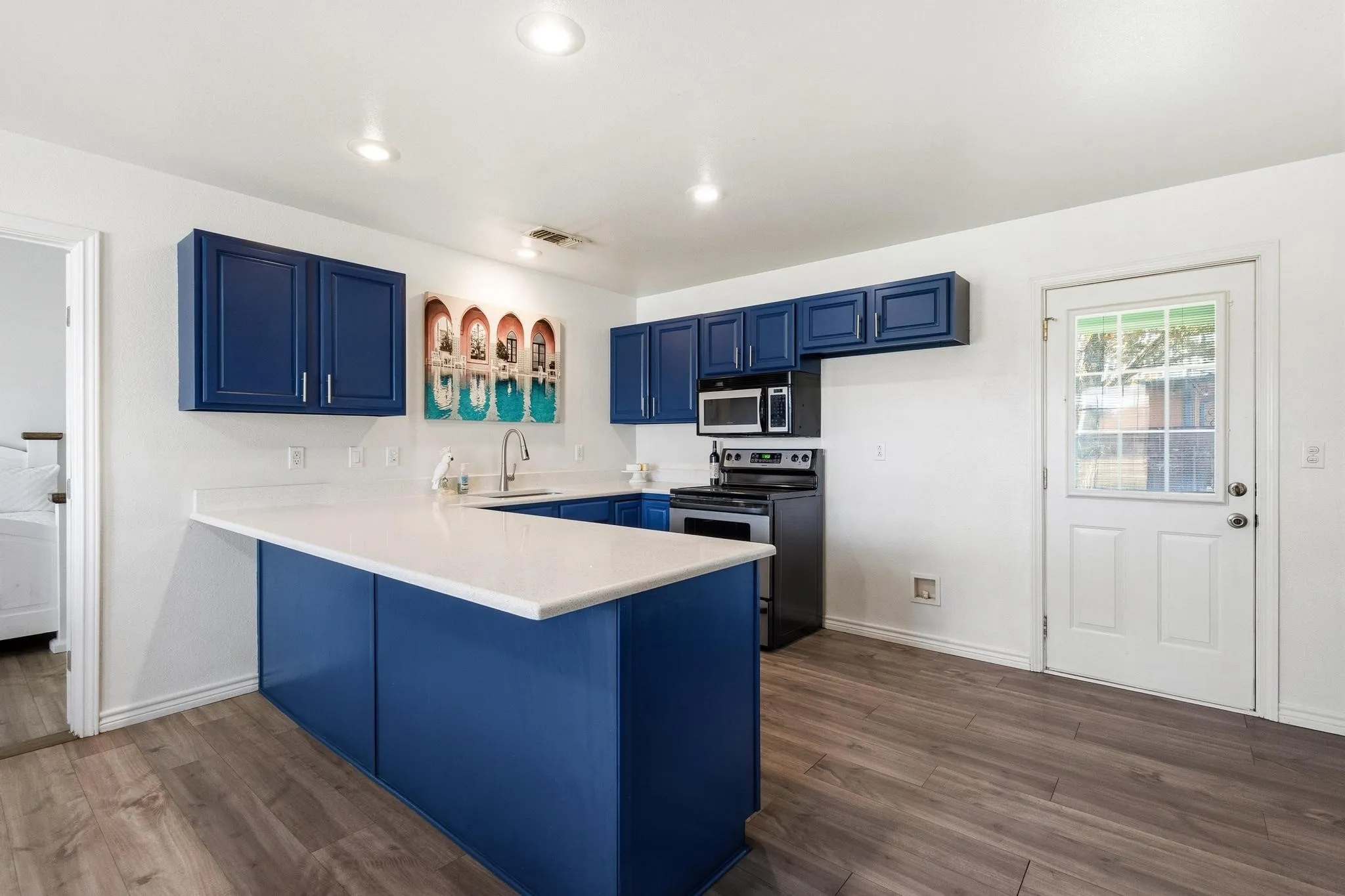 Kitchen with blue cabinets, a peninsula, stainless steel appliances, dark wood-style floors, and a kitchen bar